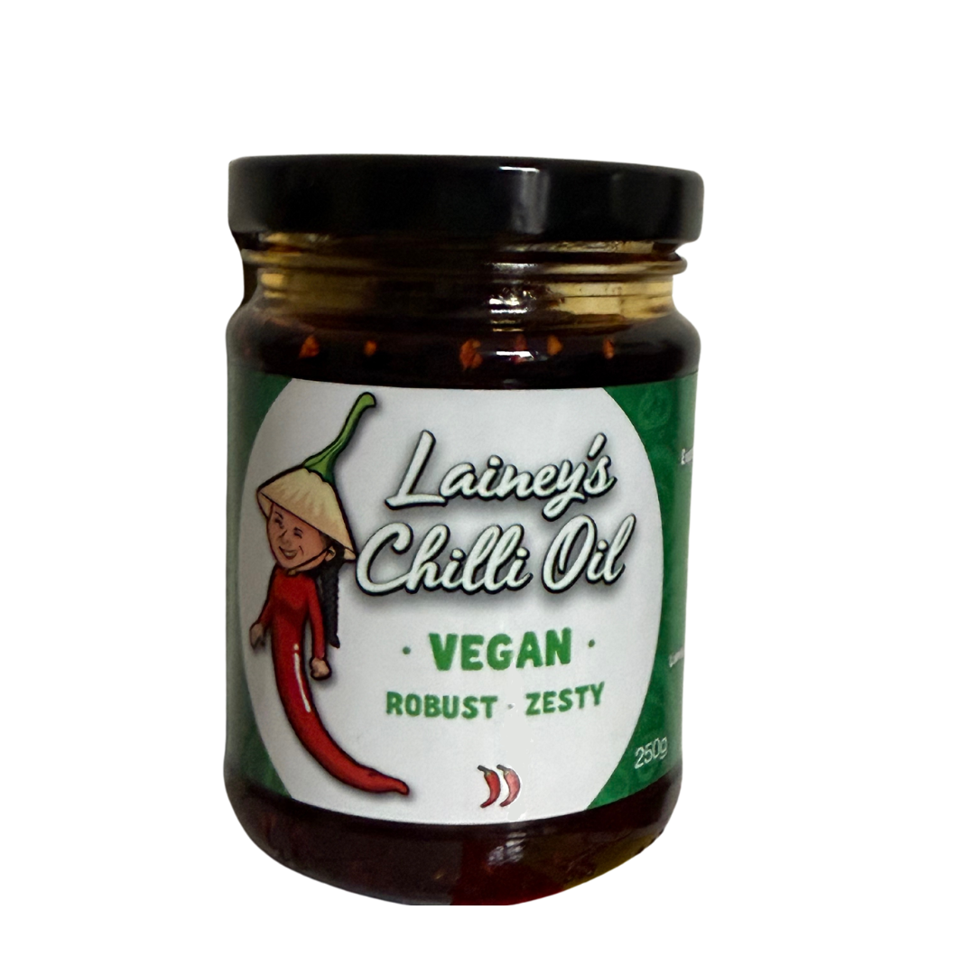 A jar of Lainey's Chili Oil labeled vegan with descriptions 'robust' and 'zesty', featuring a cartoon red chili pepper with a face, wearing a traditional Asian conical hat.
