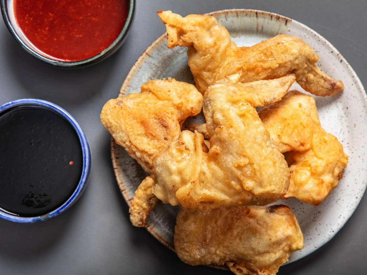Fried chicken pieces on a platter with two cups of dipping sauces, one red and one dark.