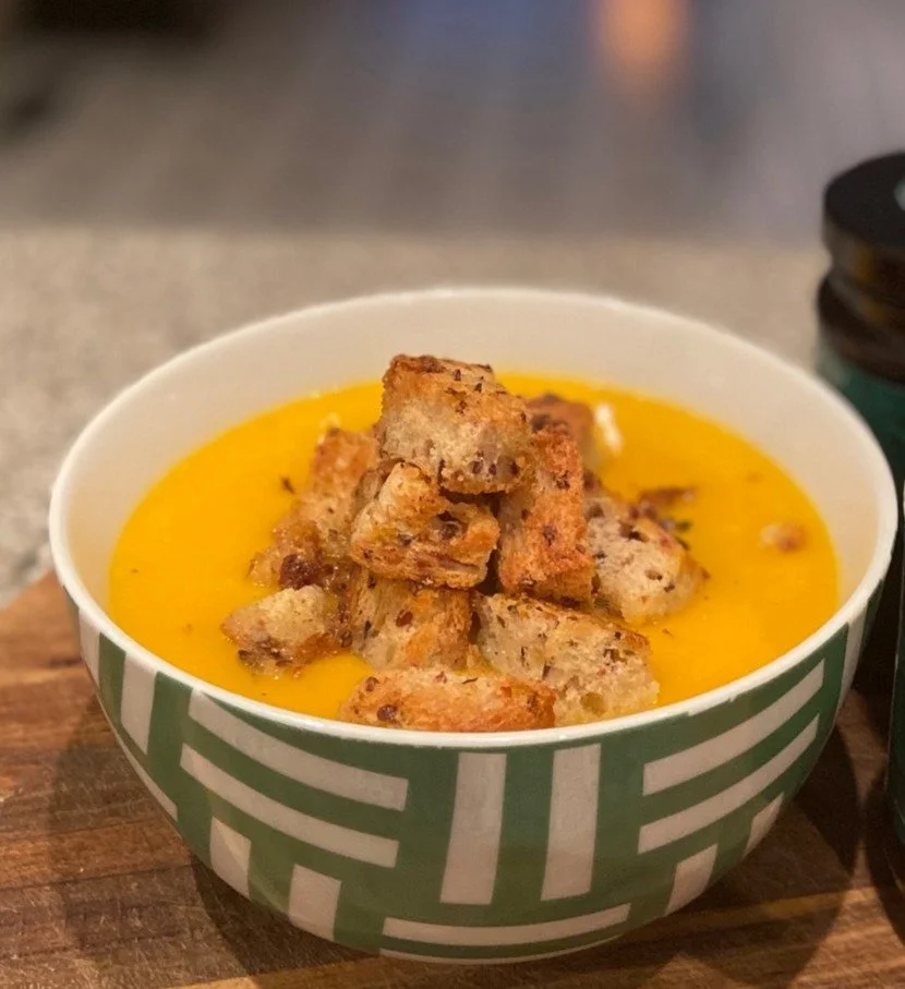 Pumpkin soup topped with toasted bread croutons in a patterned bowl on a wooden surface.