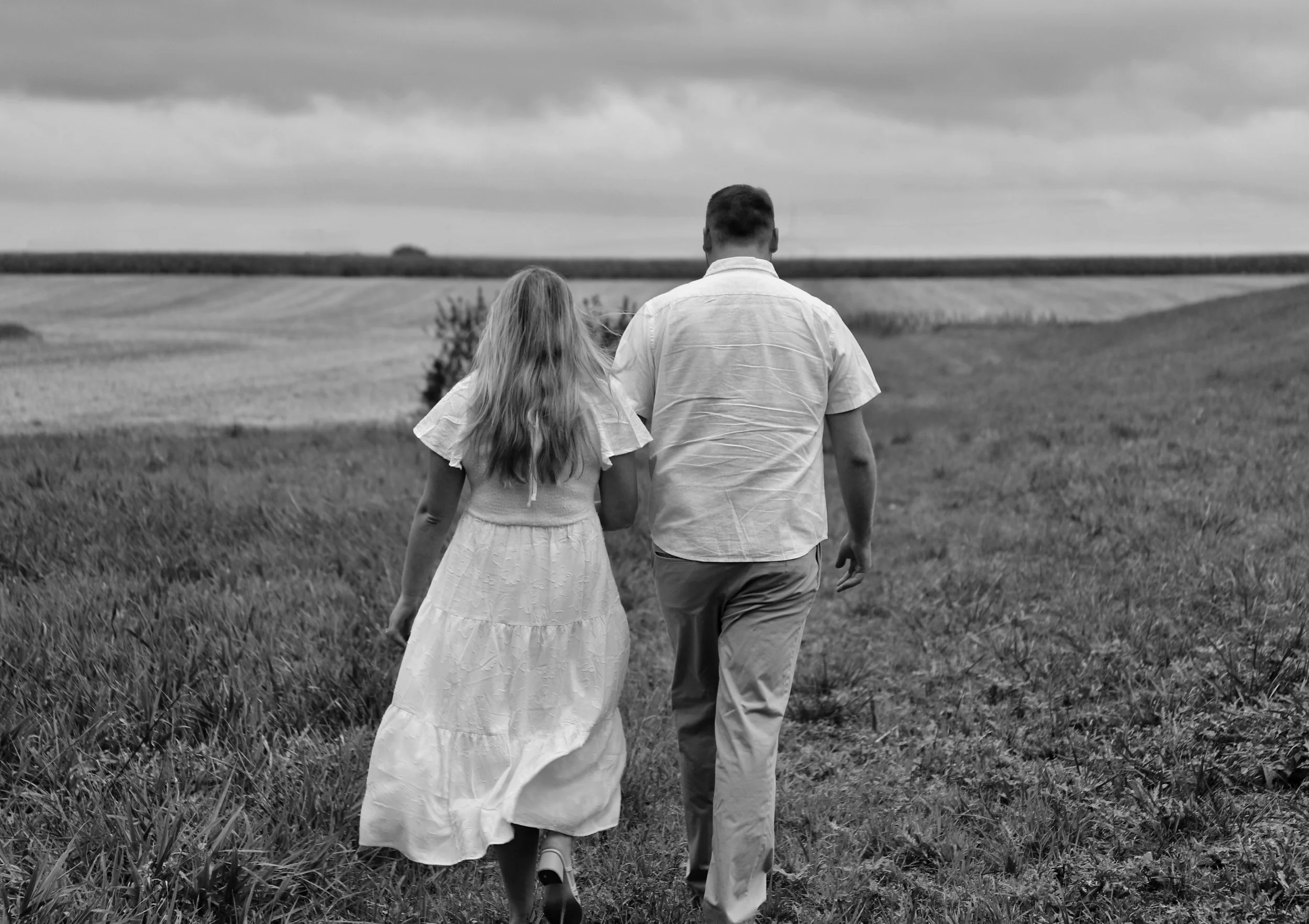 A man and woman walking together on a grassy field with overcast skies in the background.