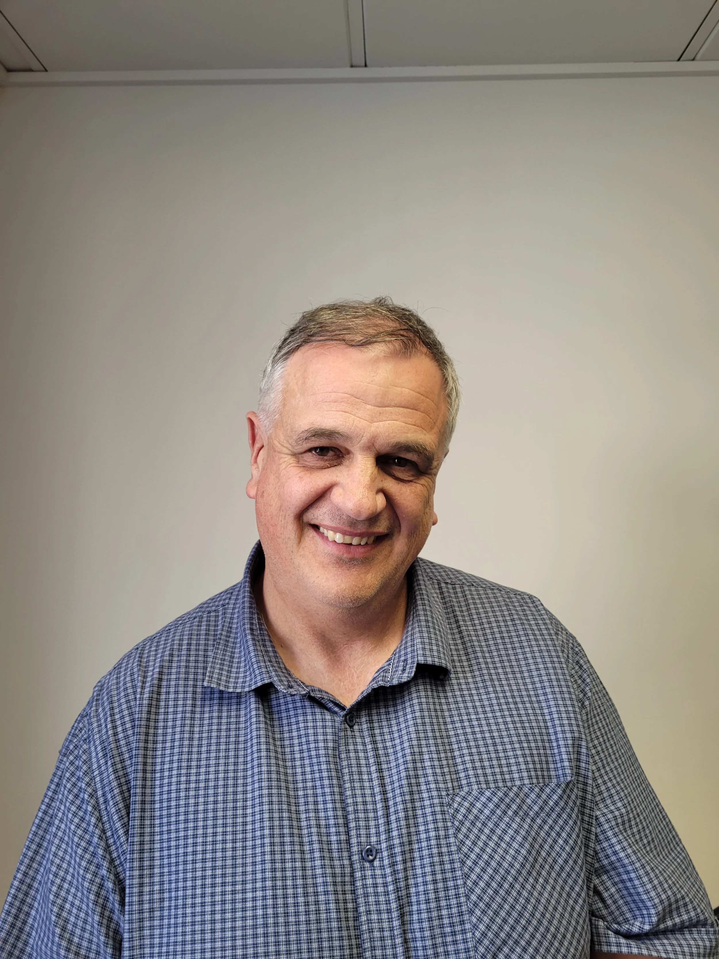 A smiling white man with grey hair wearing a check button-up shirt