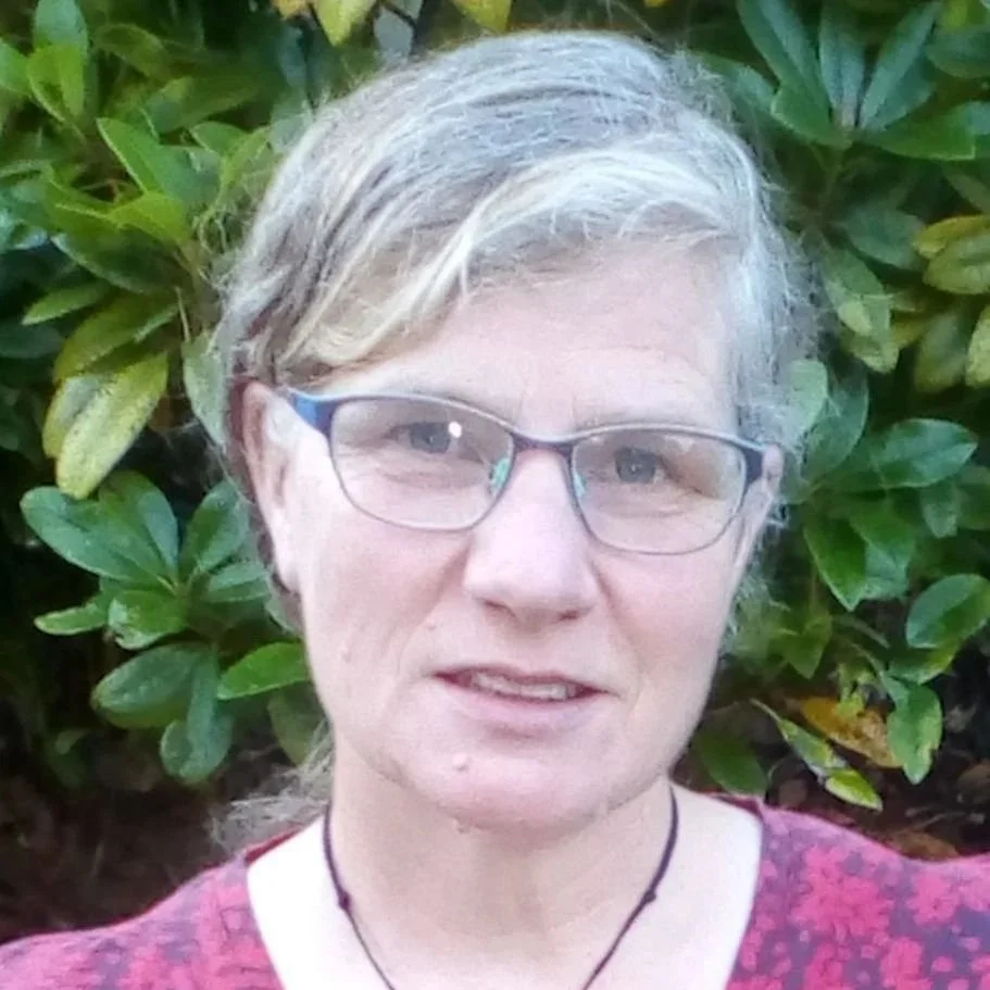 A photo of a white woman with grey hair and glasses looking at the cameraunset