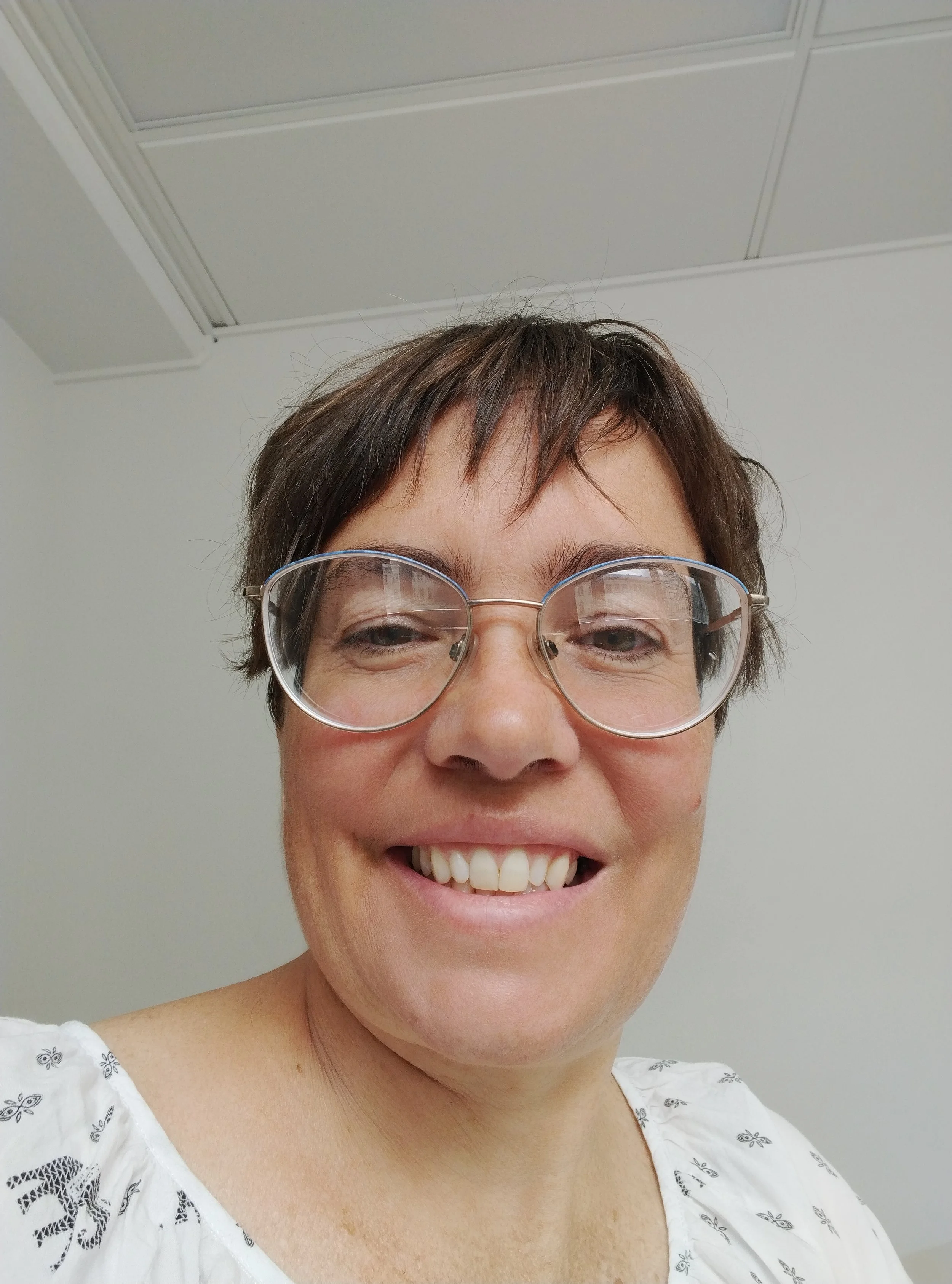 A close-up of a smiling white woman with glasses and short brown hair