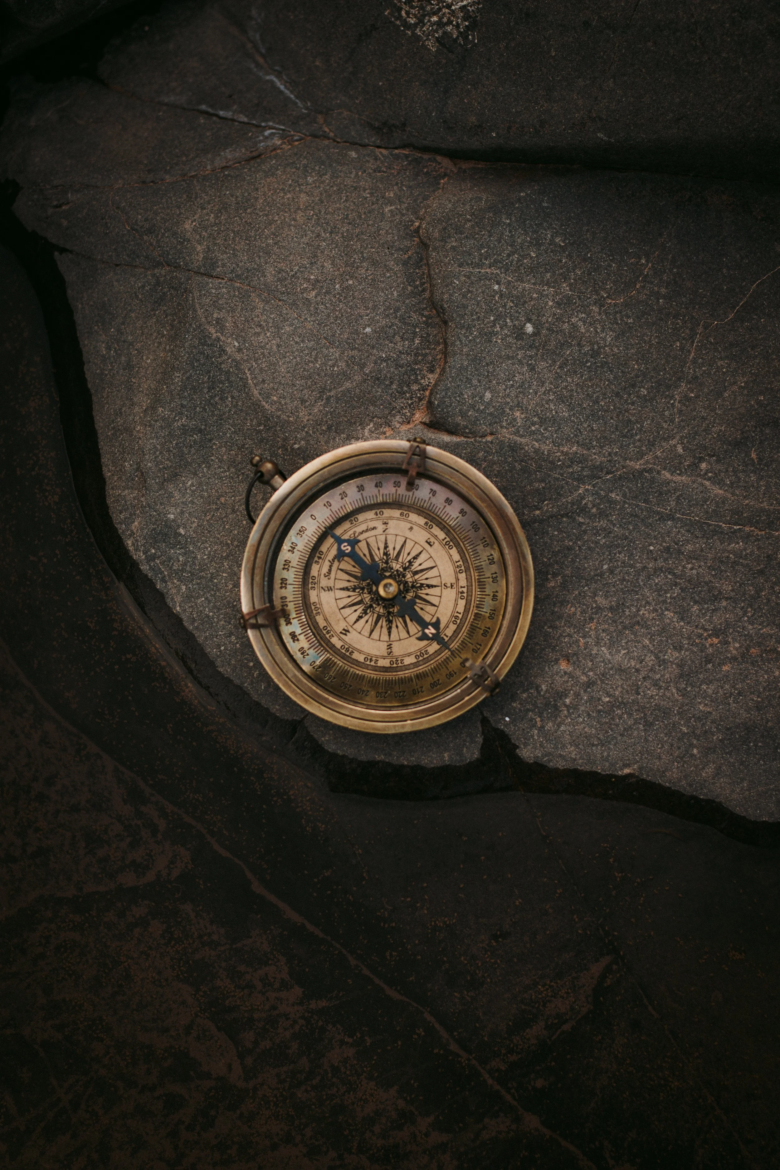 An antique brass compass resting on dark, cracked stone surface.