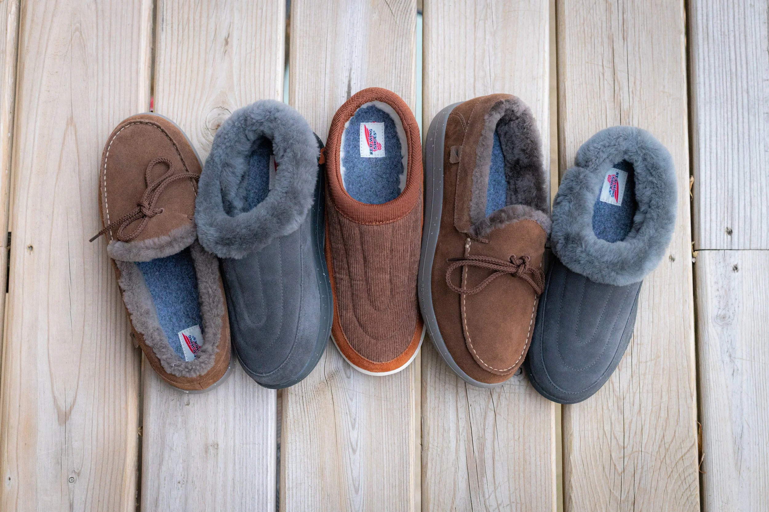 Three pairs of insulated moccasin-style slippers with plush lining, arranged on a wooden floor.