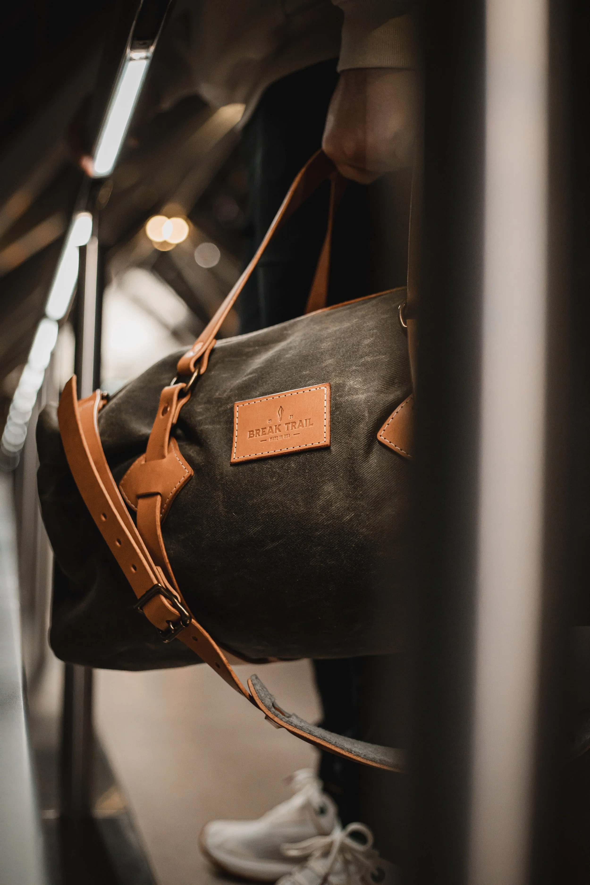 A black duffel bag with tan leather accents hanging from a luggage rack on a bus.