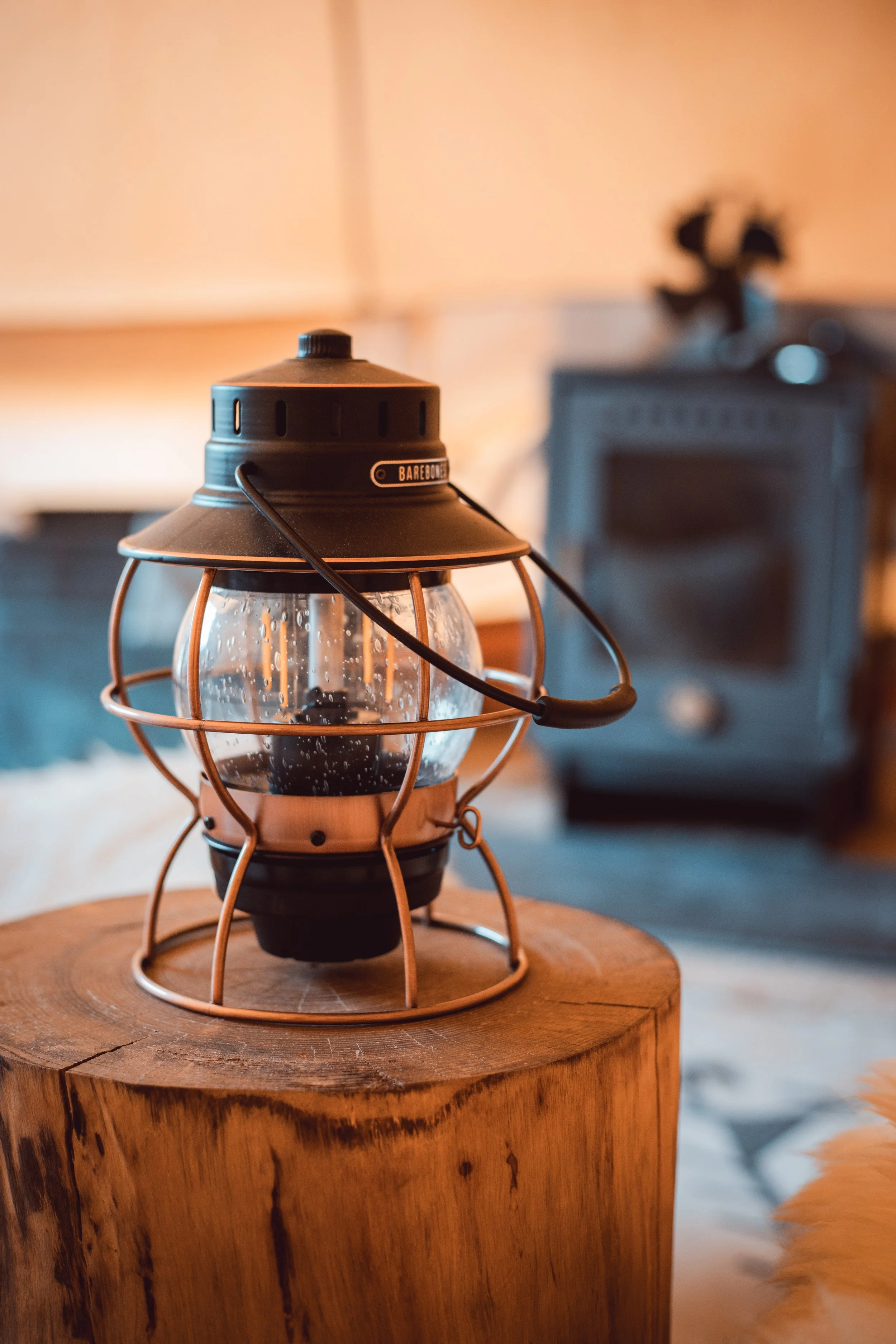 A portable lantern with a glass enclosure and metal handle, placed on a wooden surface in an indoor setting.