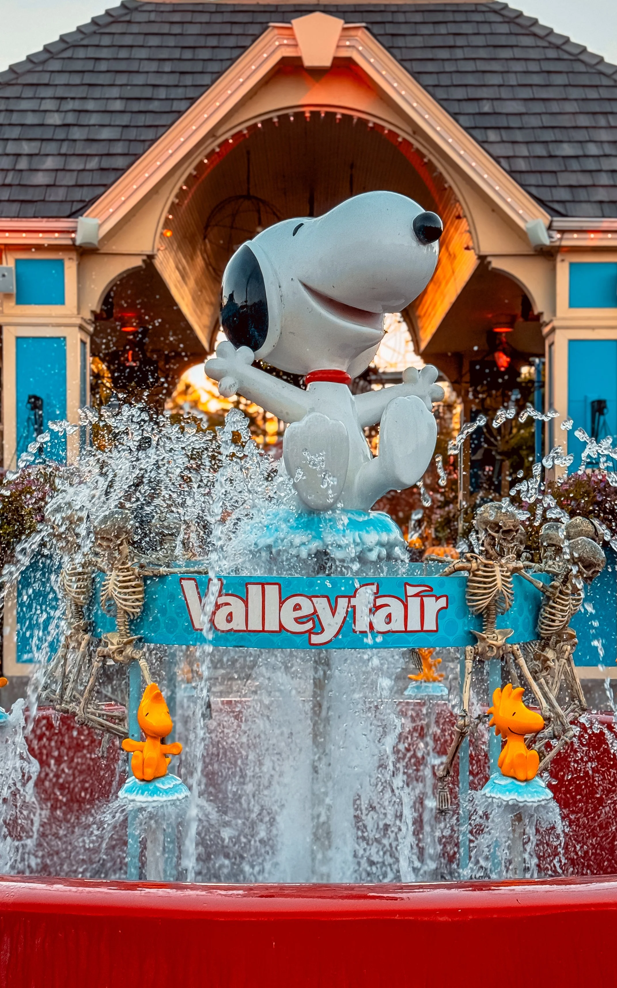Snoopy statue in a water fountain at Valleyfair amusement park, with skeleton decorations and a sign reading 'Valleyfair' behind the fountain.