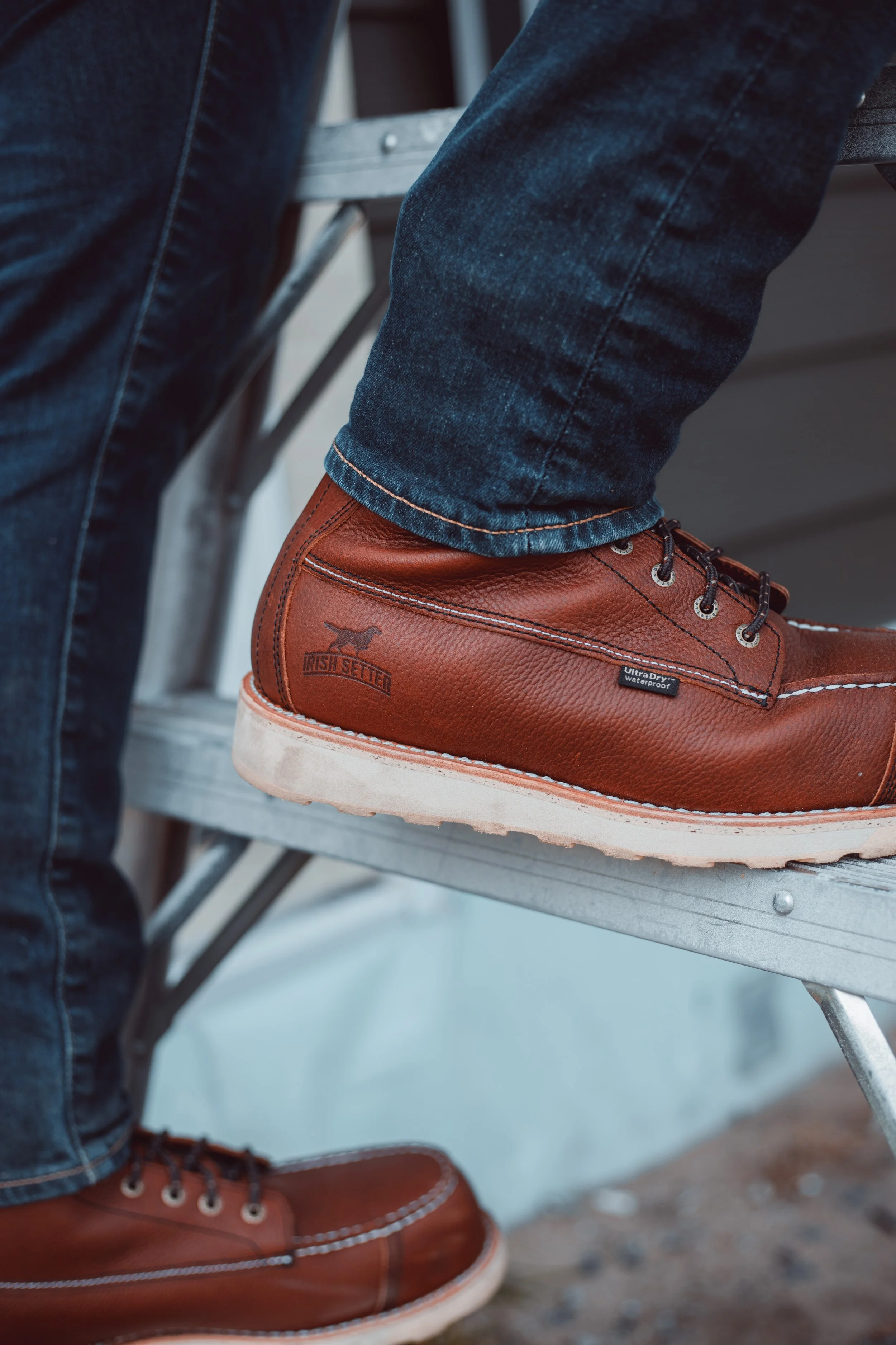 Close-up of a person's brown leather Irish Setter work boots on a metal ladder step, with jeans visible.