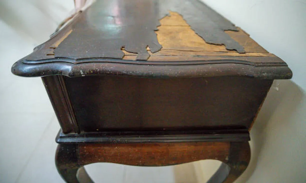 Close-up of an old wooden side table with severely peeling and cracked finish on the top surface, exposing the bare wood underneath.