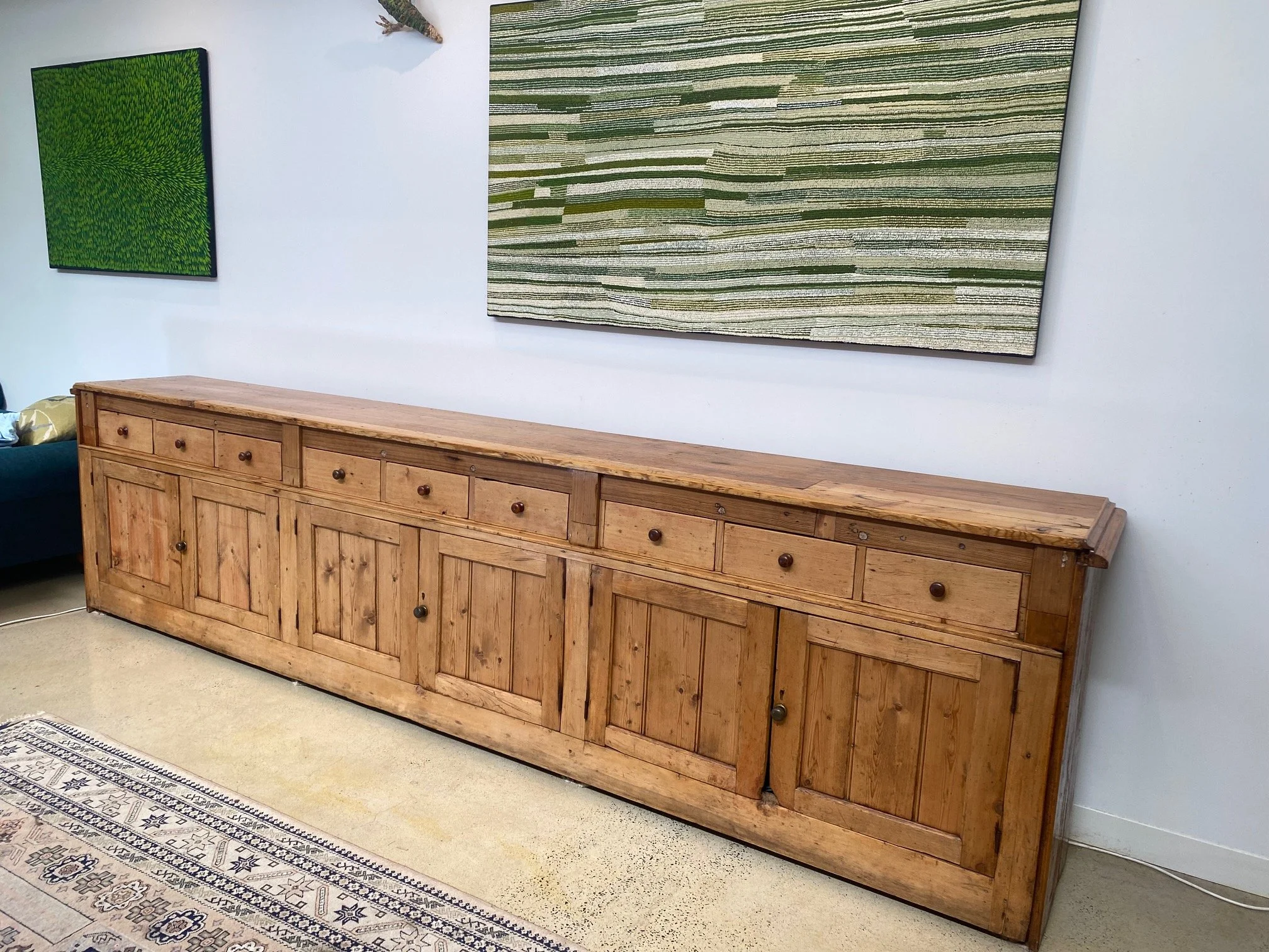 A long wooden sideboard with multiple drawers and cabinet doors, placed against a white wall with three framed abstract art pieces hanging above it.