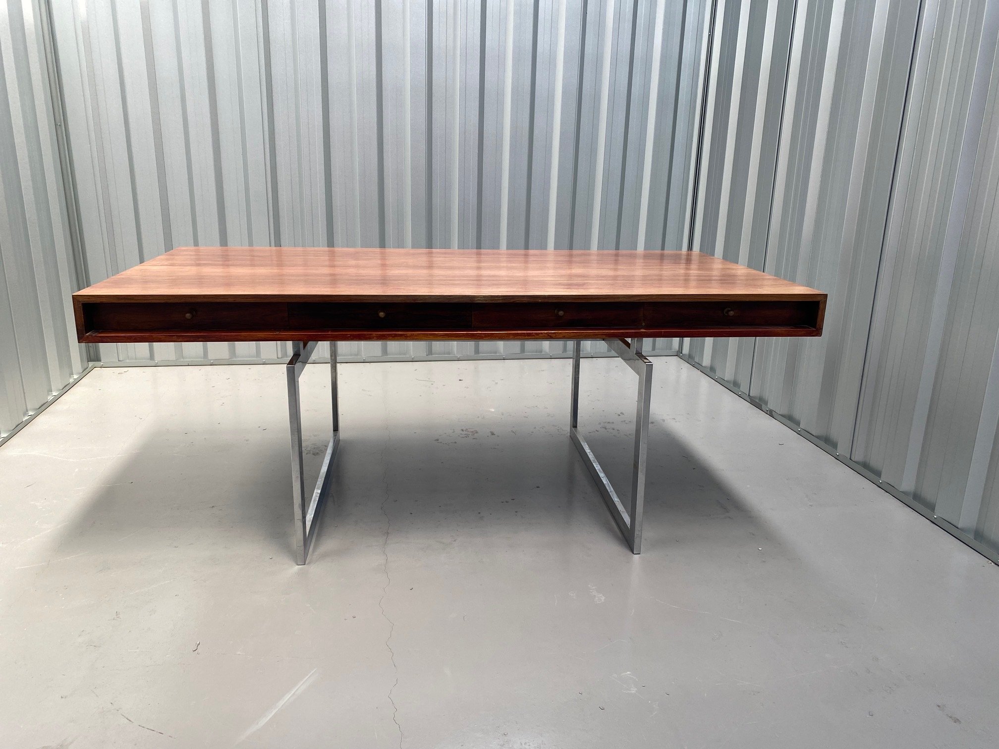 Wooden desk with metal legs in a storage unit with metal walls and concrete floor.