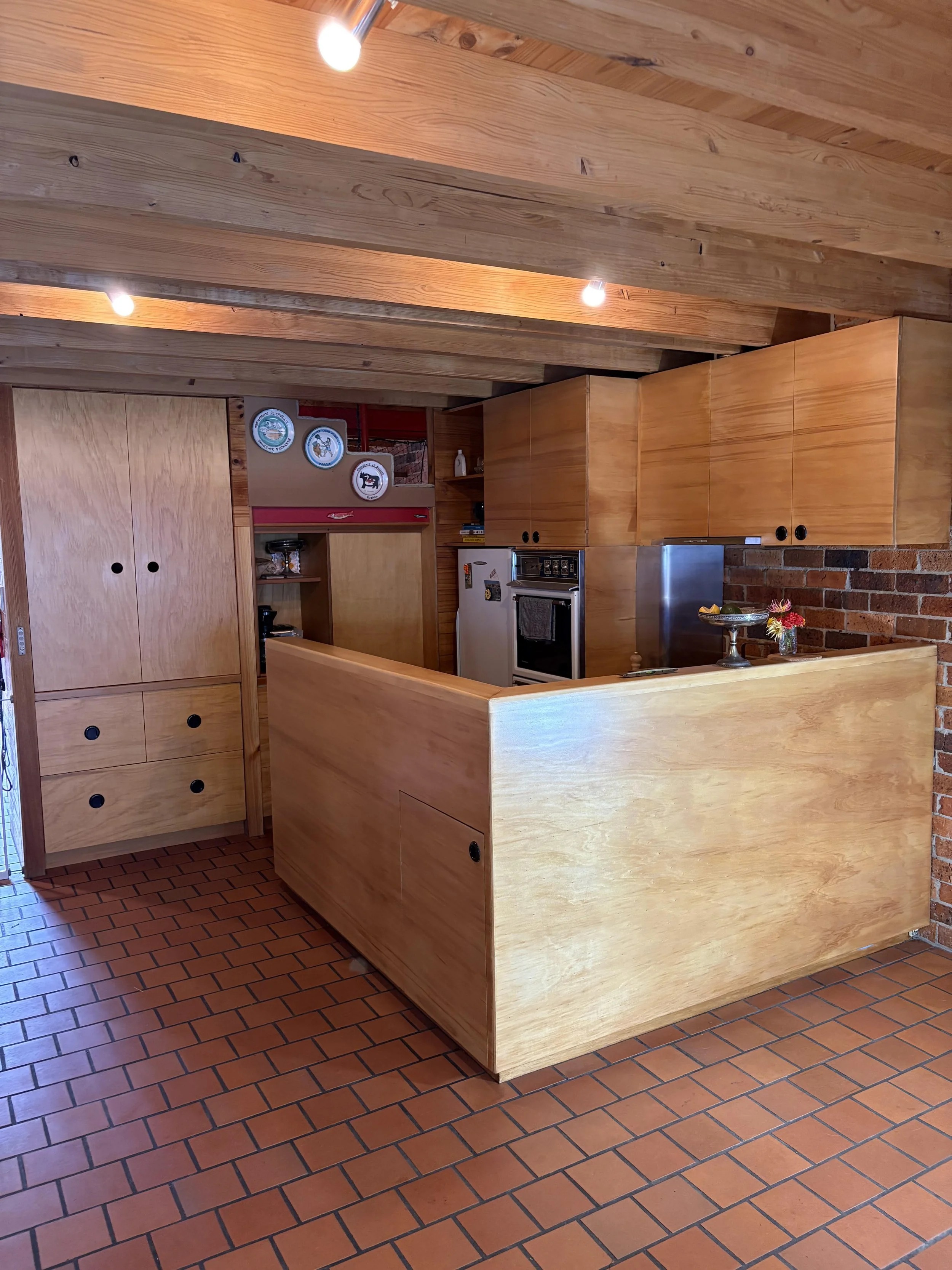 Kitchen with wooden cabinets, brick wall, tile floor, and ceiling beams, featuring appliances and decorative plates.