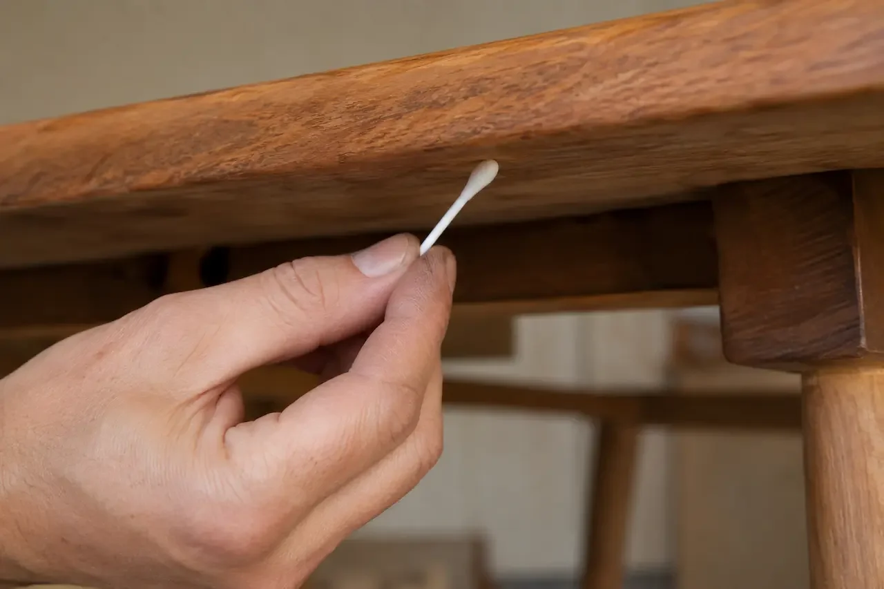 Testing an indoor teak finish with acetone on a cotton bud beneath a table top