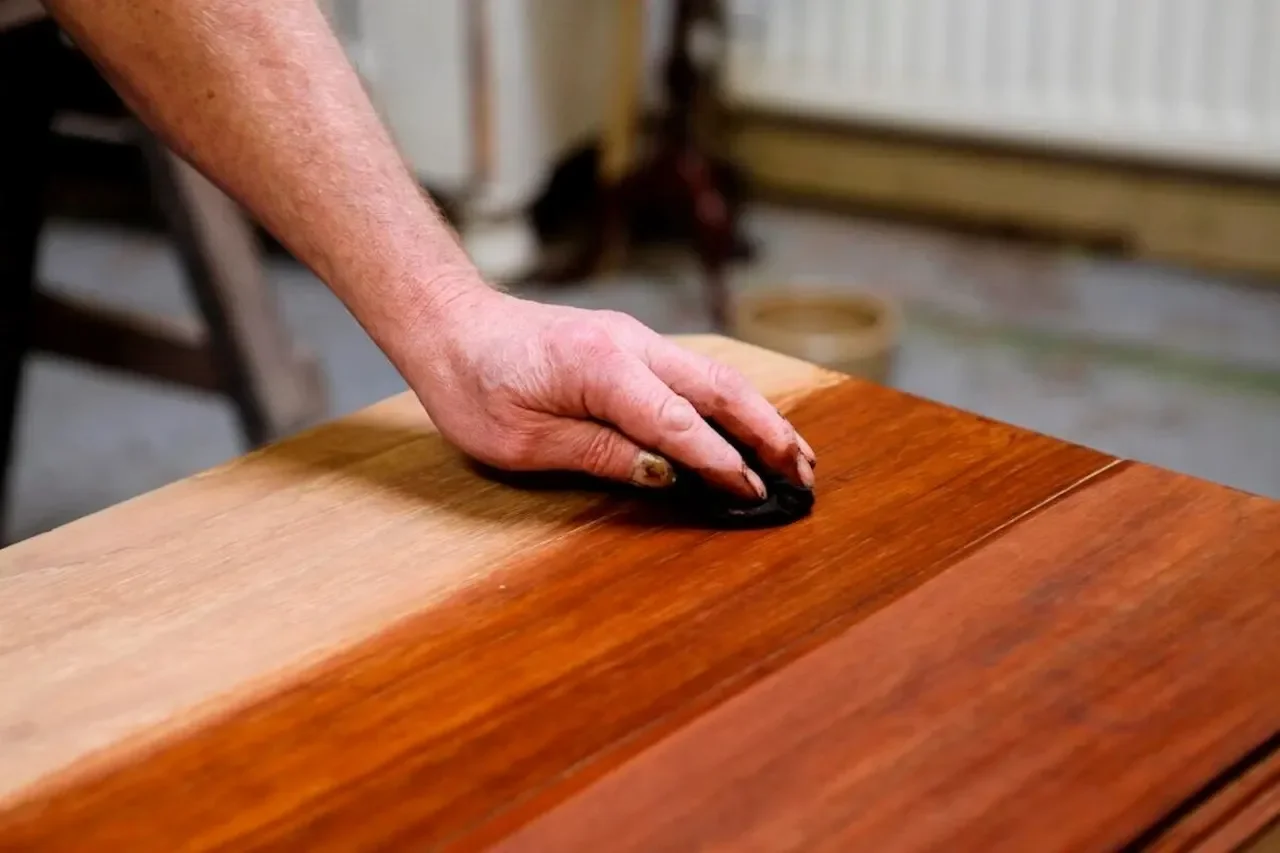 Hand applying wood stain finish on a wooden furniture surface during restoration process
