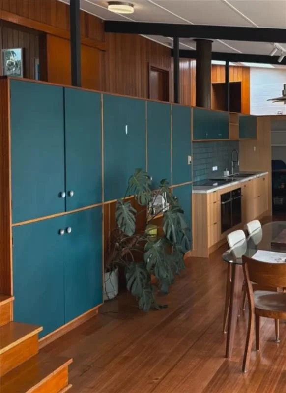 Kitchen with teal cabinets, wooden countertops, a dining table with chairs, and a tall leafy houseplant.