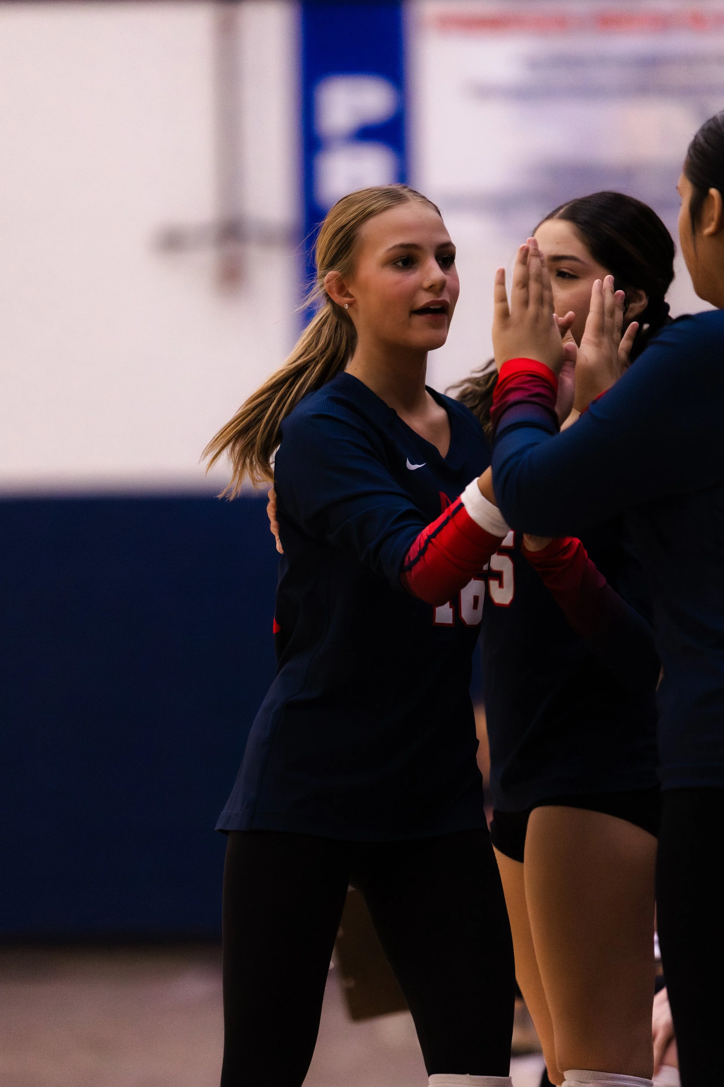 A young woman in a volleyball uniform giving a high five to her teammates during a game in an indoor gymnasium.