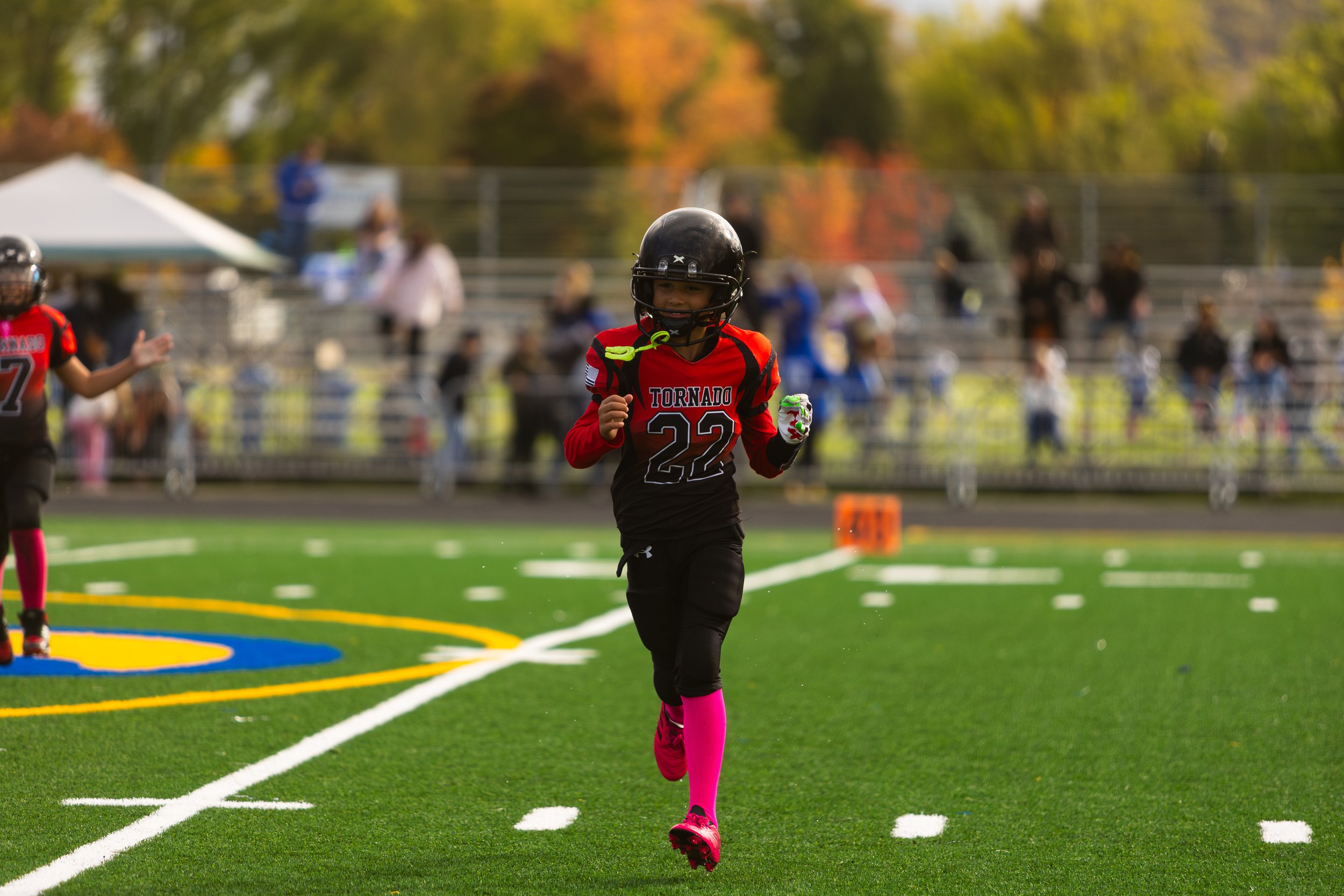 A young football player wearing number 22 and a red and black uniform running on a field with a crowd in the background.