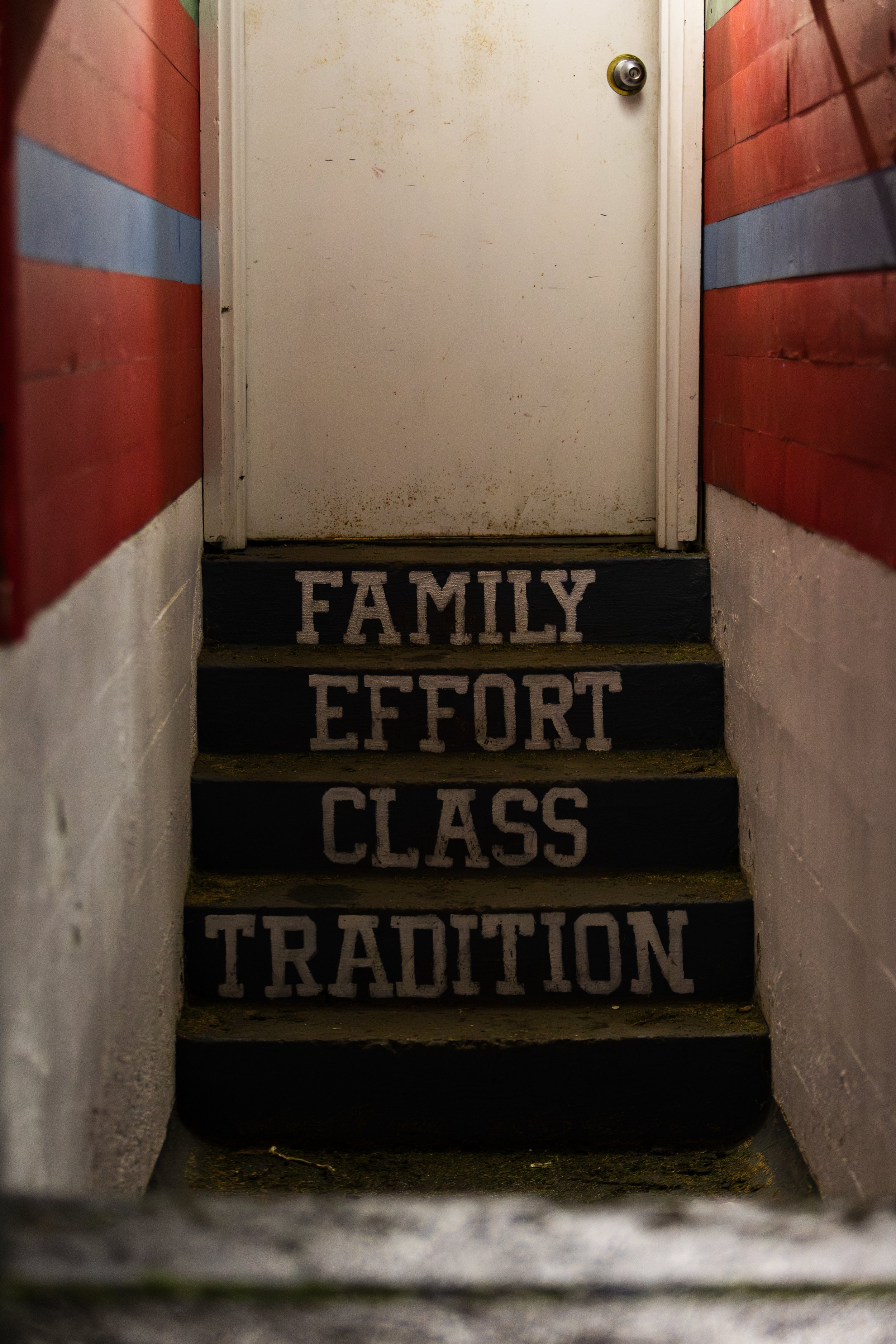 Stairs with words painted on each step: "Family," "Effort," "Class," and "Tradition" leading to a closed white door.