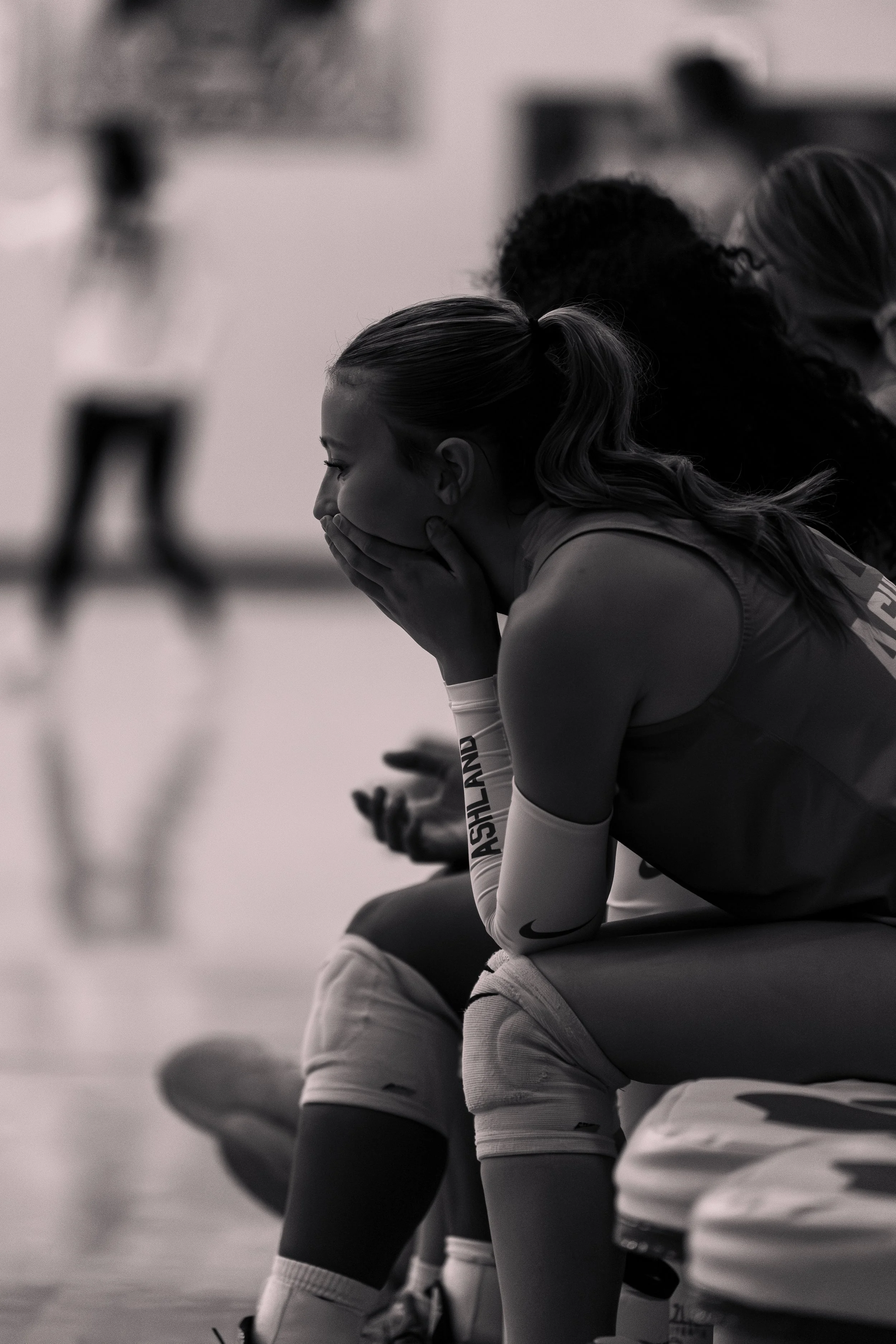 Female athlete sitting on a bench with her hands covering her face in a sports setting.