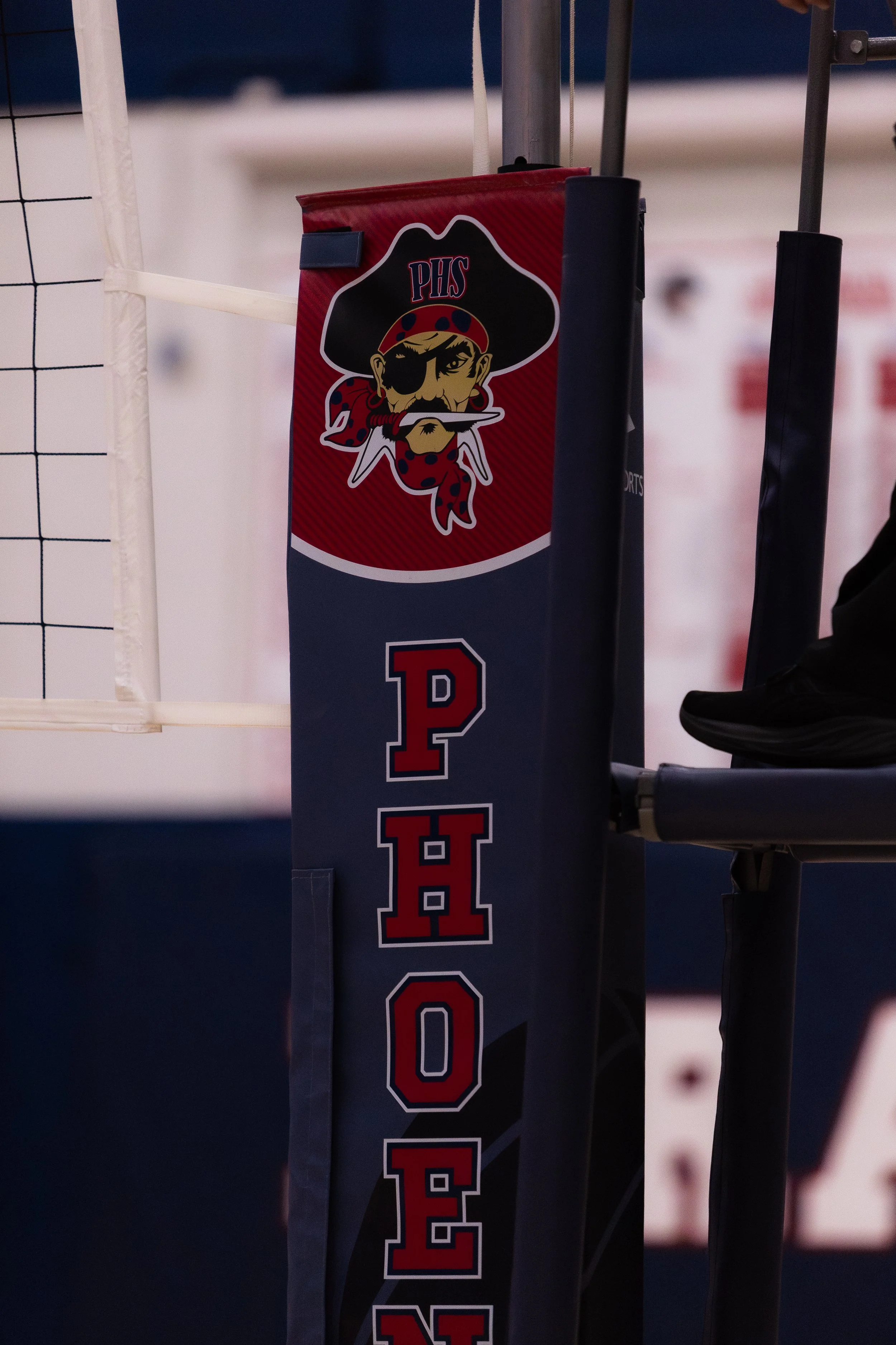 A volleyball net with a flag displaying a pirate mascot and the word 'PHOENIX' on a volleyball court.