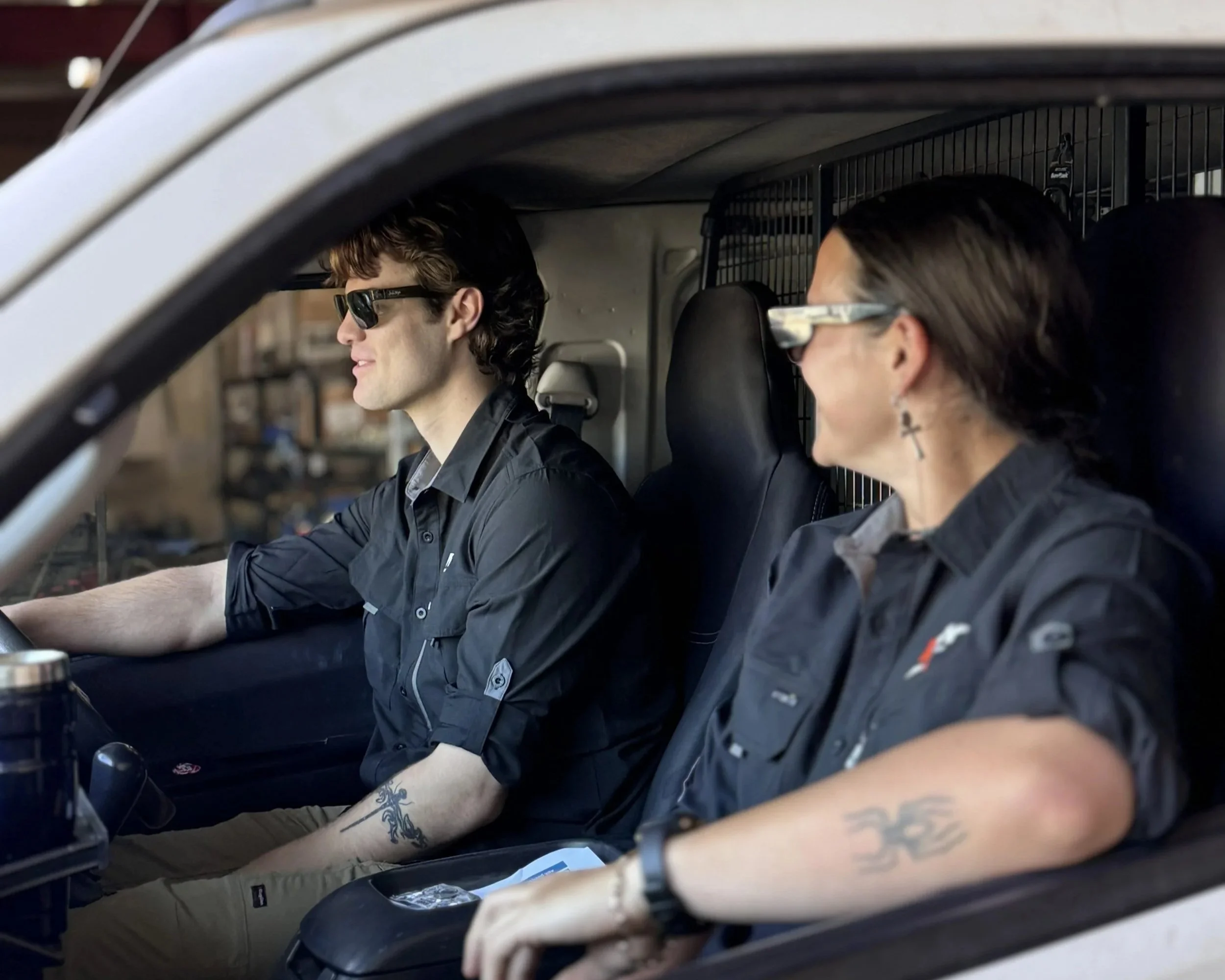 Two plumbers sitting in a vehicle in Belmont WA, one driving and the other sitting beside them, wearing black shirts.