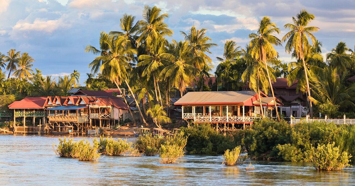 The Mekong riverbank on Don Khon, where stilted houses and guesthouses sit beneath coconut palms.