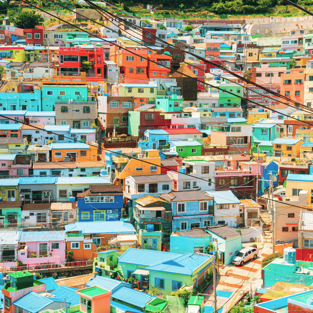 Colorful densely packed hillside neighborhood with houses painted in various bright colors, including blue, green, pink, yellow, and red, with overhead power lines crossing the scene.