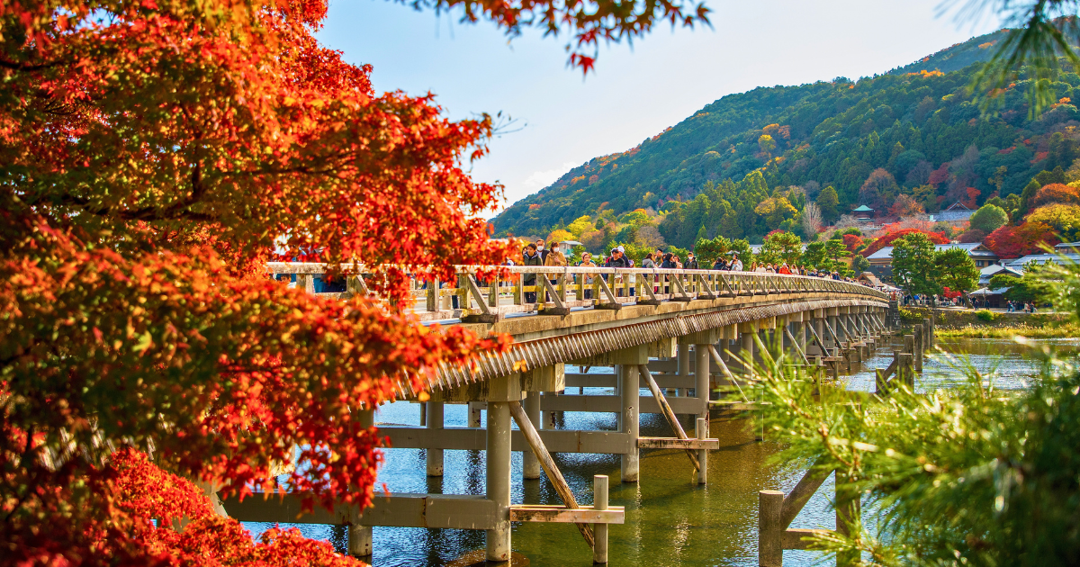 The Togetsukyo bridge crossing the Katsura River with autumn maples in the foreground and the Arashiyama hills behind