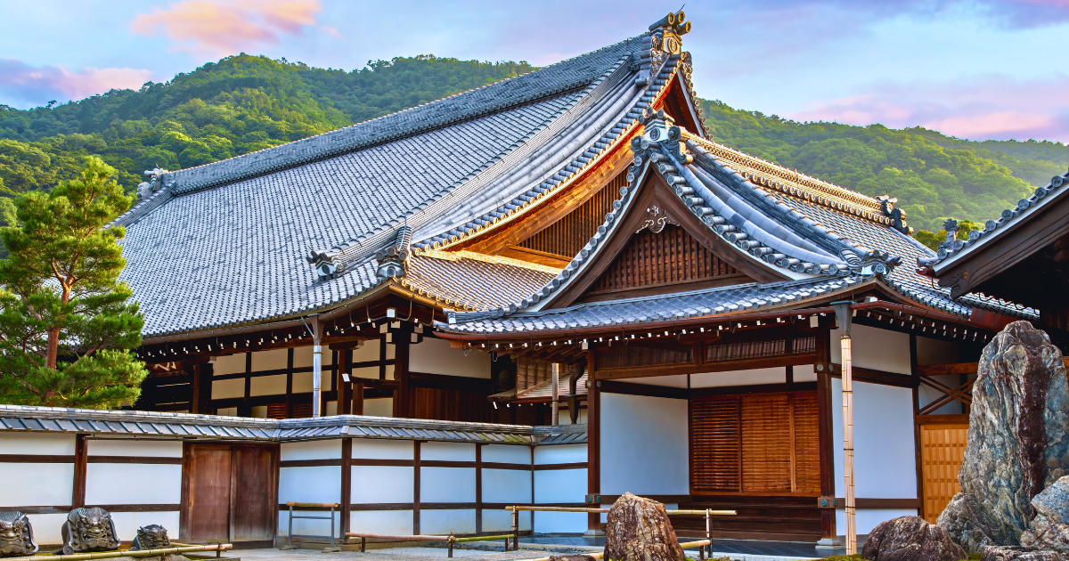 Tenryu-ji temple building with traditional tiled roof and the wooded Arashiyama hills rising behind