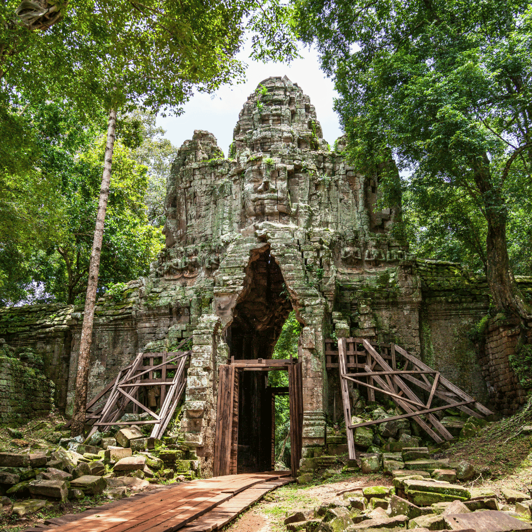 Ancient stone temple with a large carved face at the entrance, surrounded by lush green trees.
