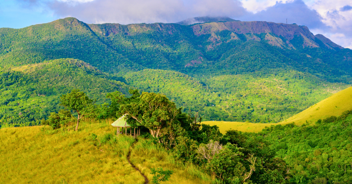 A hut and footpath on open green hills below the mountains of Busuanga