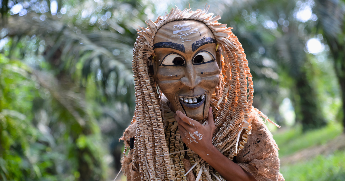 A carved wooden spirit mask worn with a woven palm-leaf costume