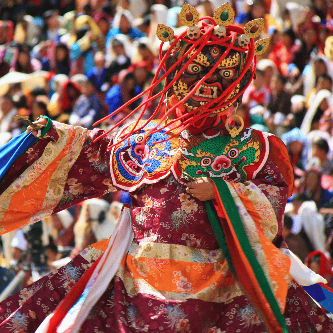 Performer wearing traditional costume and a fierce demon mask during a cultural festival, with a large crowd in the background.