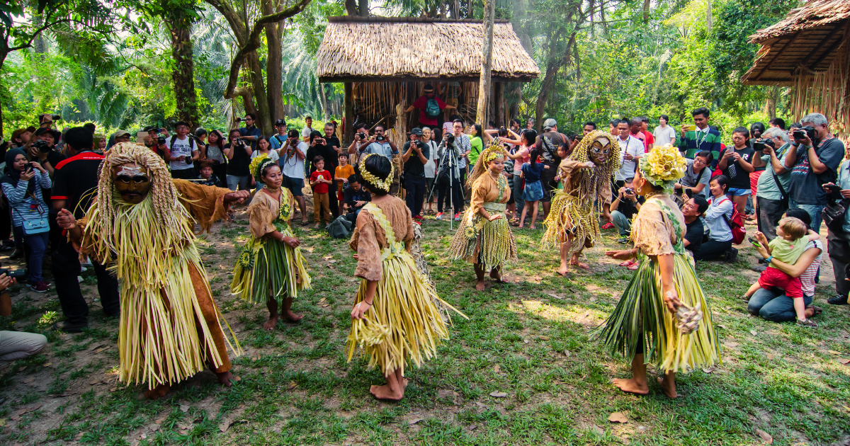 Mah Meri community members performing a traditional dance in carved masks and woven leaf costumes