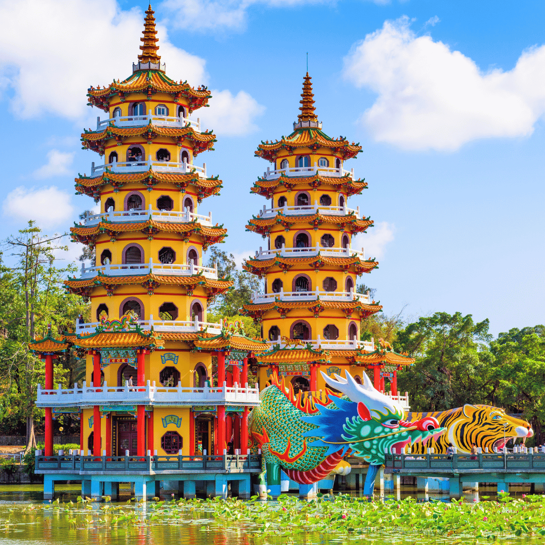 Colorful Asian temple with two pagoda towers and a dragon sculpture near water with lily pads, green trees, and blue sky in the background.