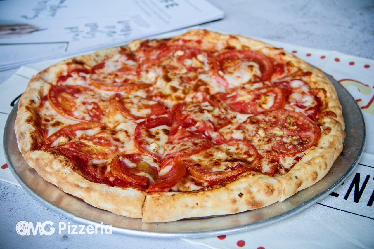 A pizza topped with tomato slices, cheese, and peppers on a metal tray.