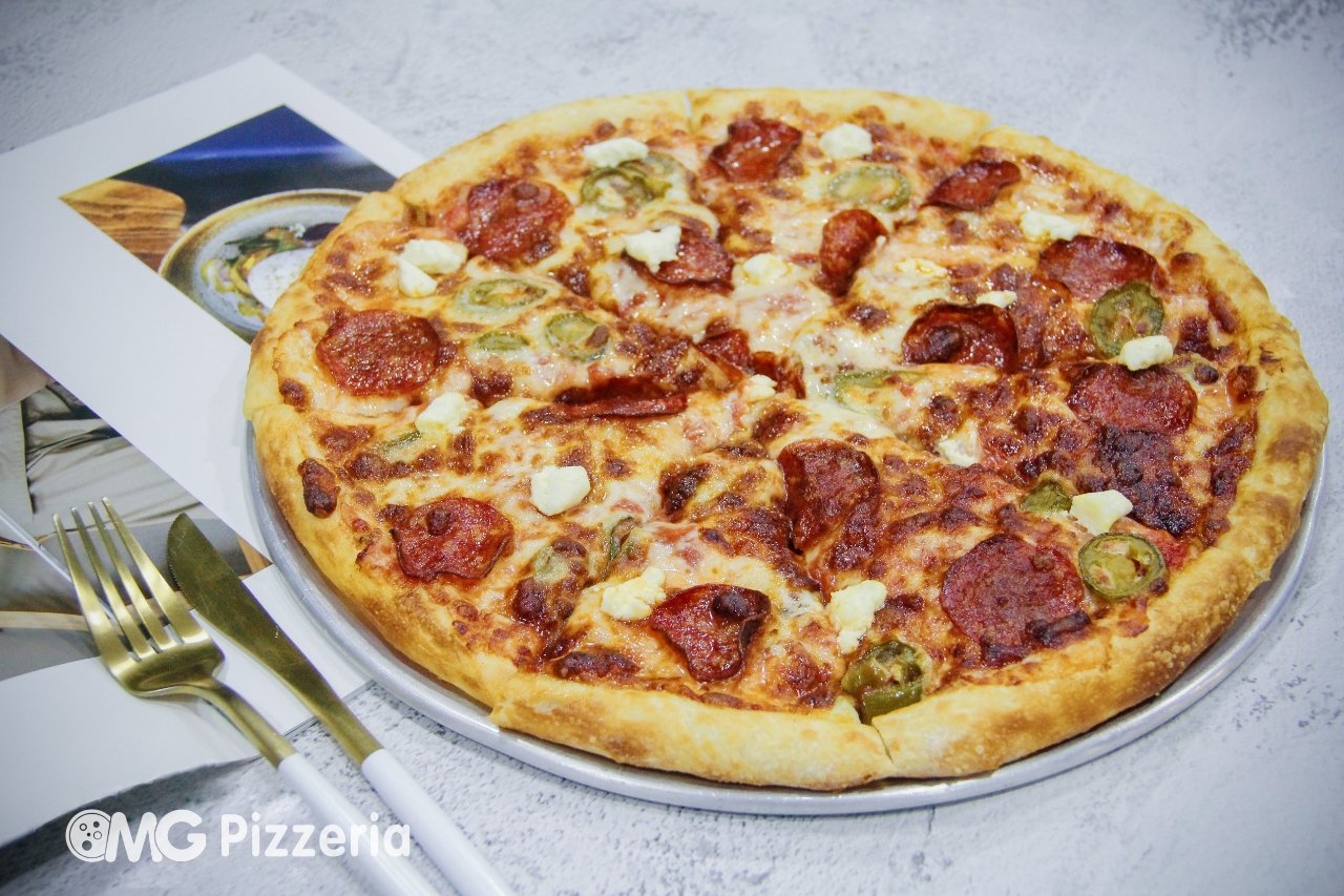 A pepperoni and jalapeno pizza with cheese on a metal tray, with a gold fork and knife, and a magazine under the tray