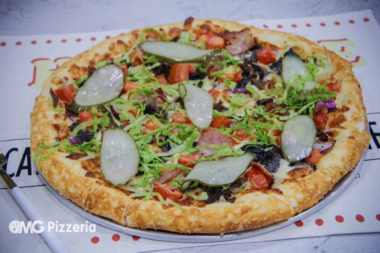 Vegetarian pizza with lettuce, cucumbers, tomatoes, red onions, and olives on a golden crust.
