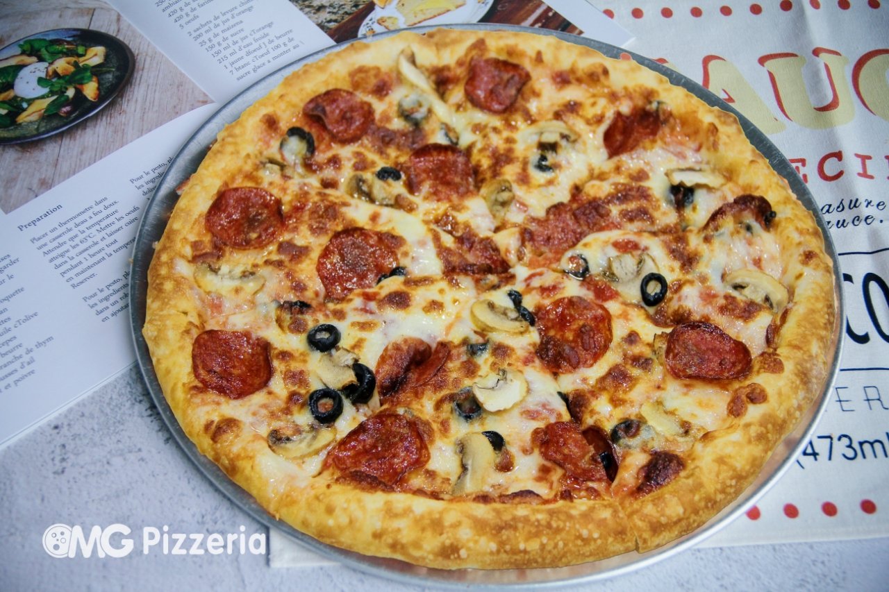 A pepperoni and mushroom pizza with black olives on a metal tray, placed on a table with menus and papers underneath.
