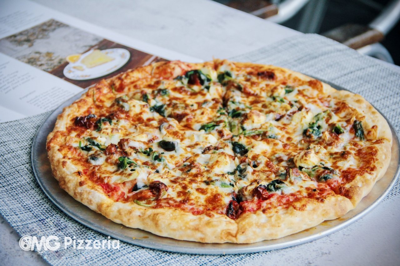 Cheese pizza with spinach and mushroom slices on a round metal tray, placed on a table with a menu in the background.