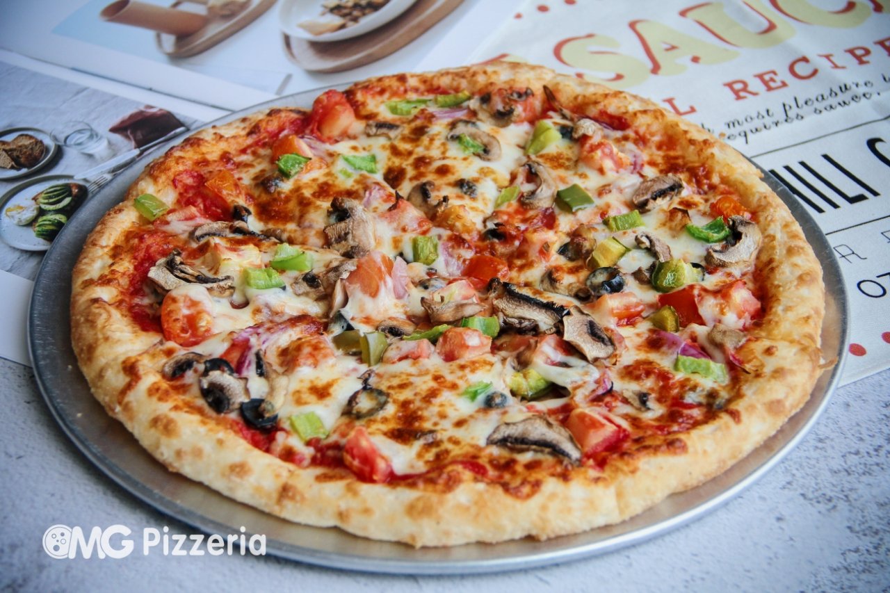 A pizza with cheese, mushrooms, green peppers, and tomatoes on a silver tray.