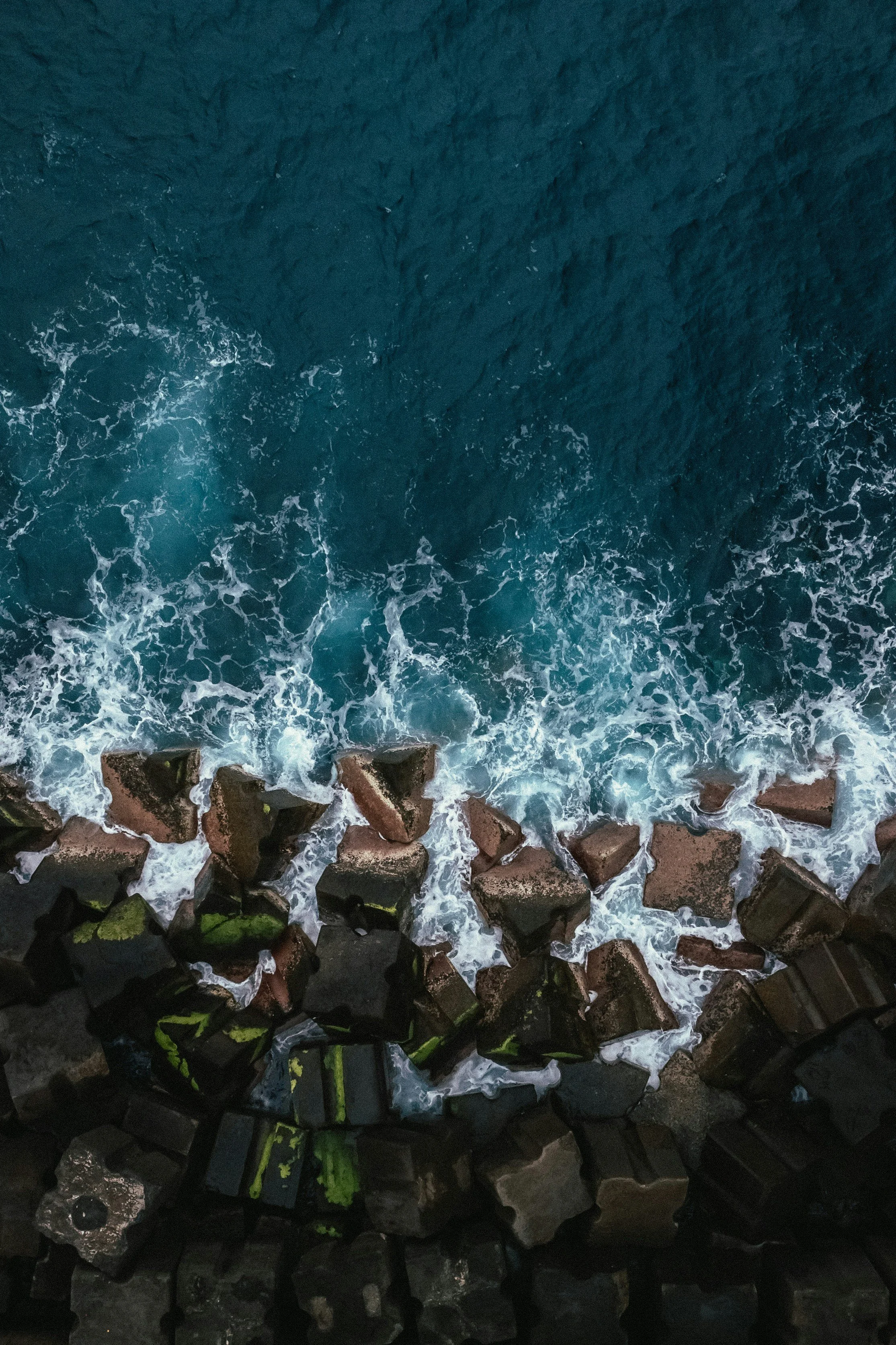 Aerial view of ocean waves crashing against a rocky breakwater.