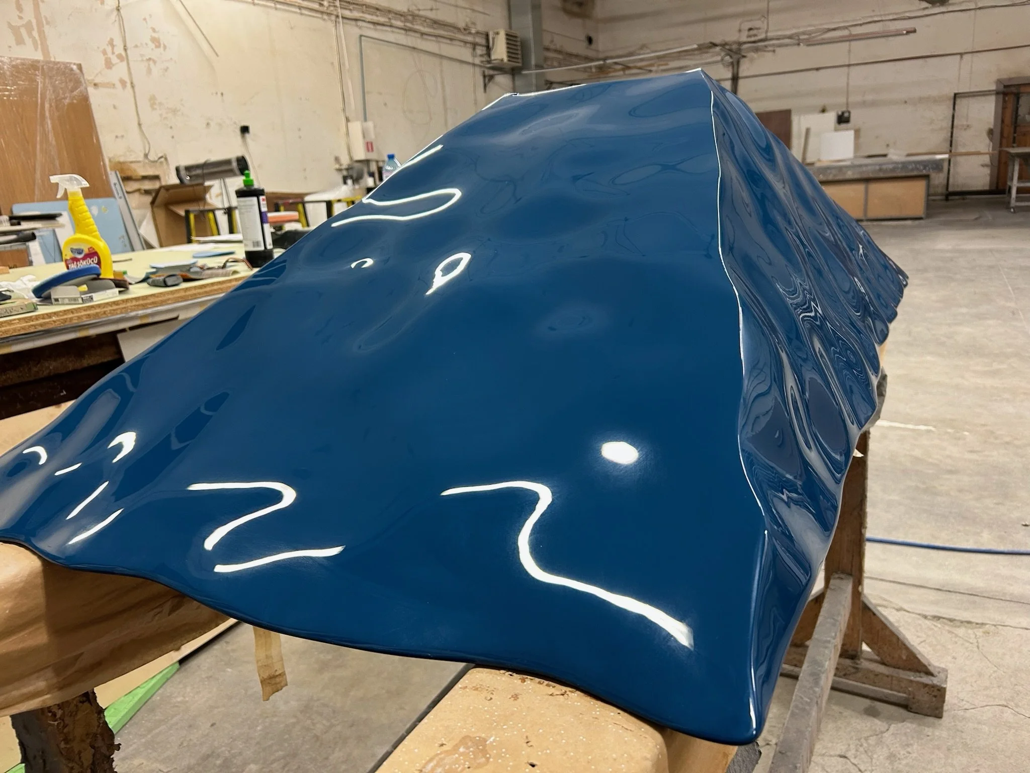 Close-up of a dark blue, glossy, curved and smooth surface in a workshop setting.