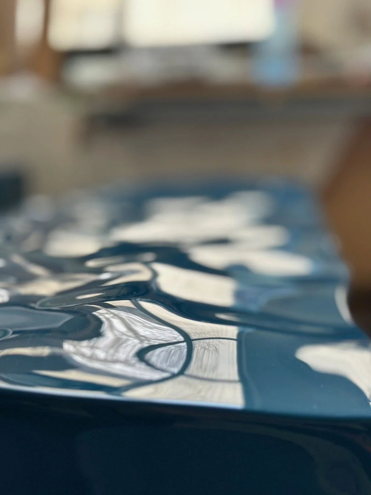 Close-up photo of a crumpled, shiny, blue surface reflecting light and nearby objects, taken at a low angle.