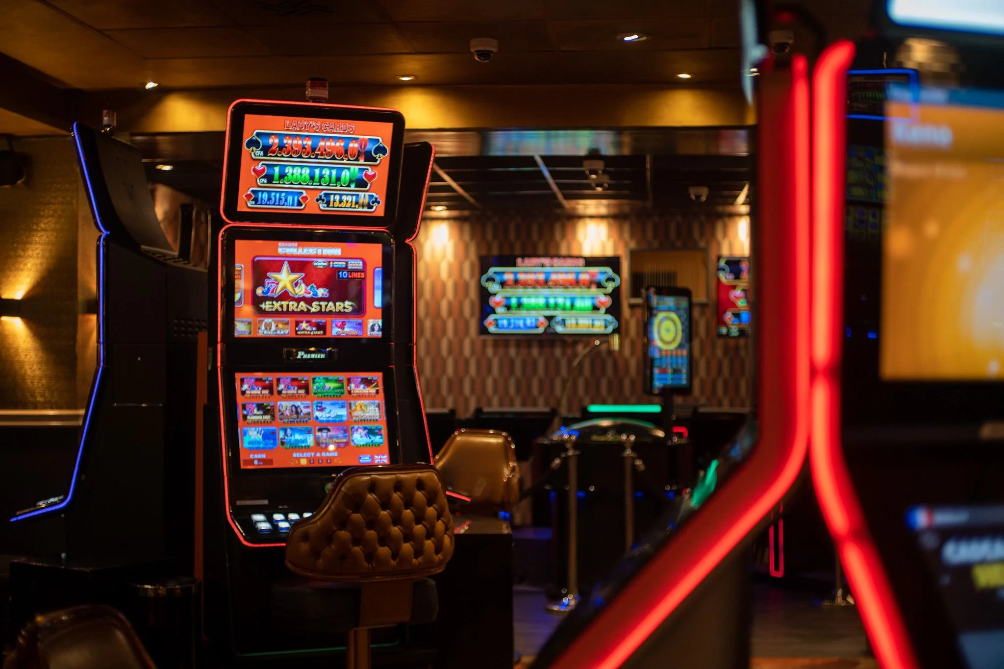 Interior of a casino with brightly lit slot machines featuring colorful graphics and digital screens, surrounded by a dimly lit atmosphere.