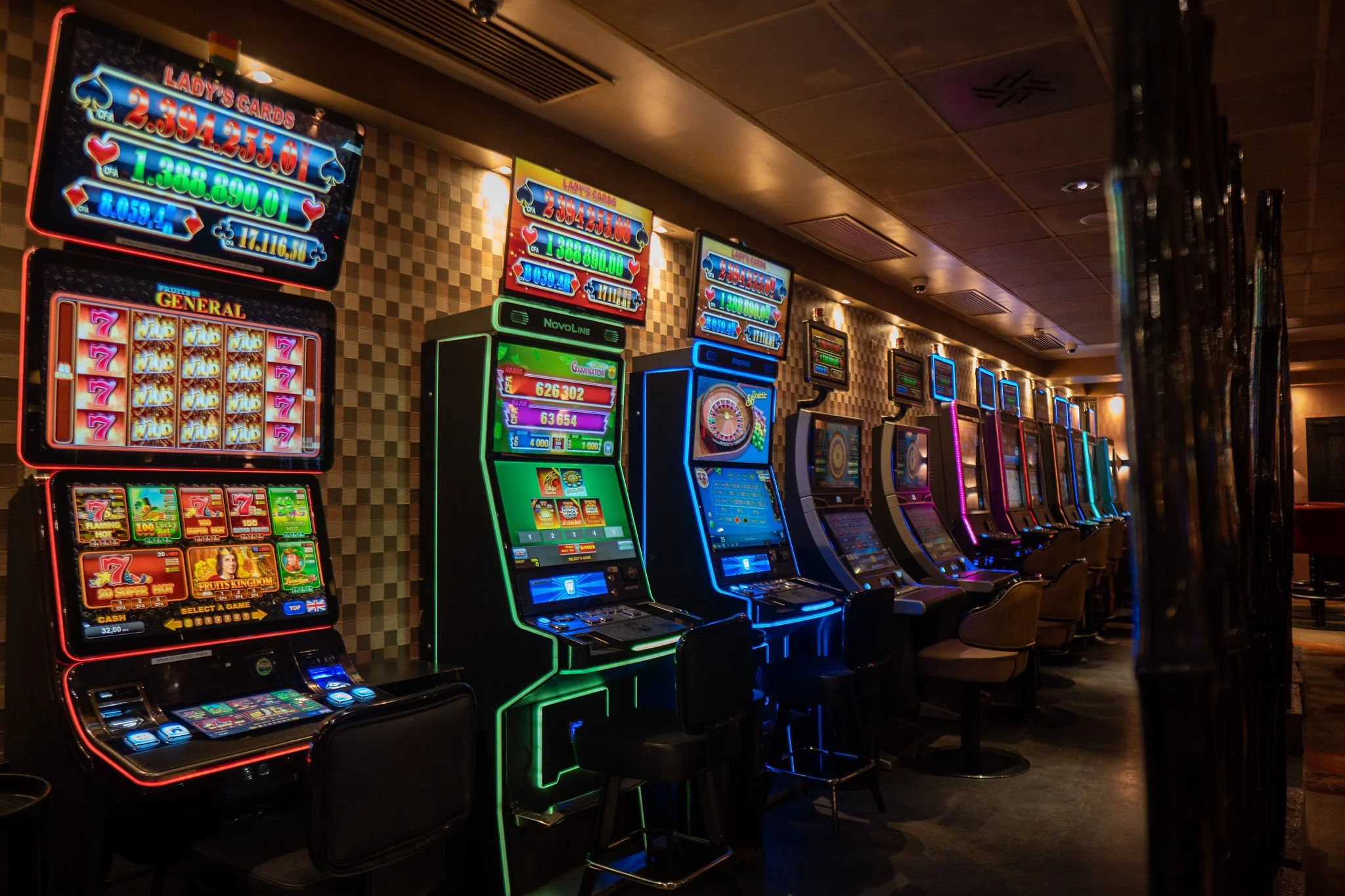 Row of brightly lit slot machines in a casino, with digital screens displaying game graphics and colorful lights.