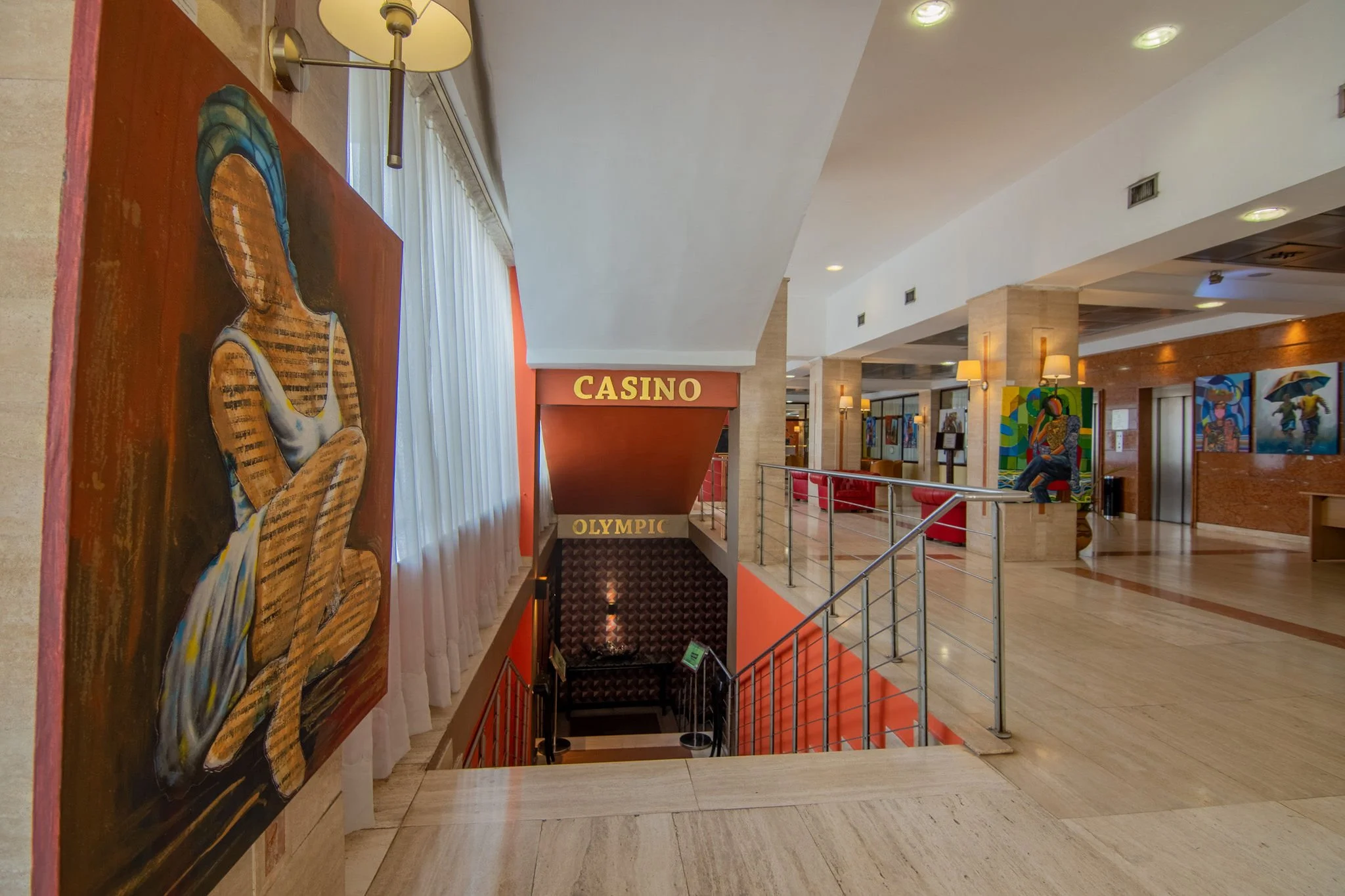 Interior view of a hotel or casino lobby with artwork, seating, and signs for a casino and Olympic