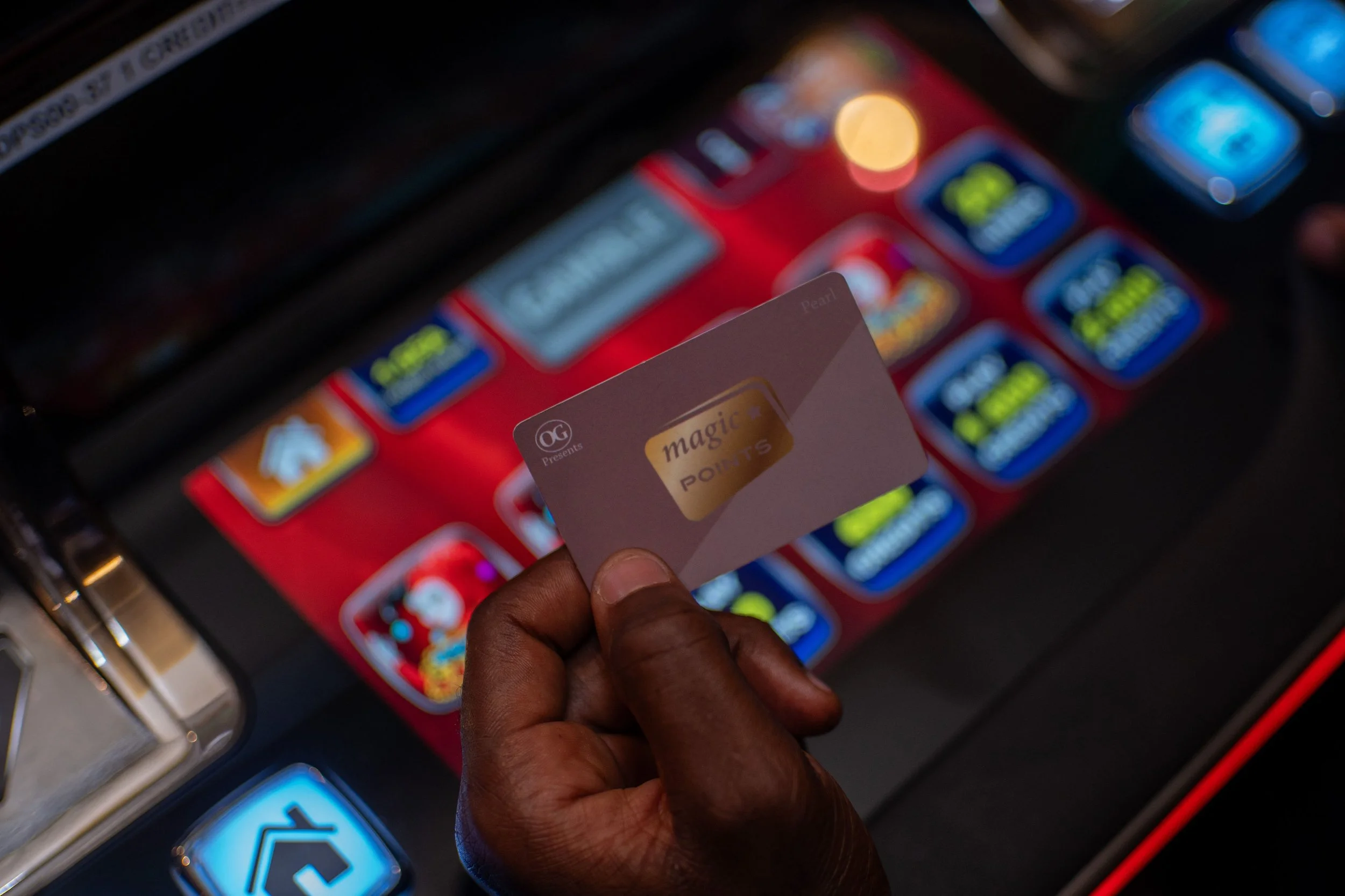 A hand holding a membership card with the words 'magic POINTS' in front of a digital gaming or vending machine with various colorful app icons on a red background.