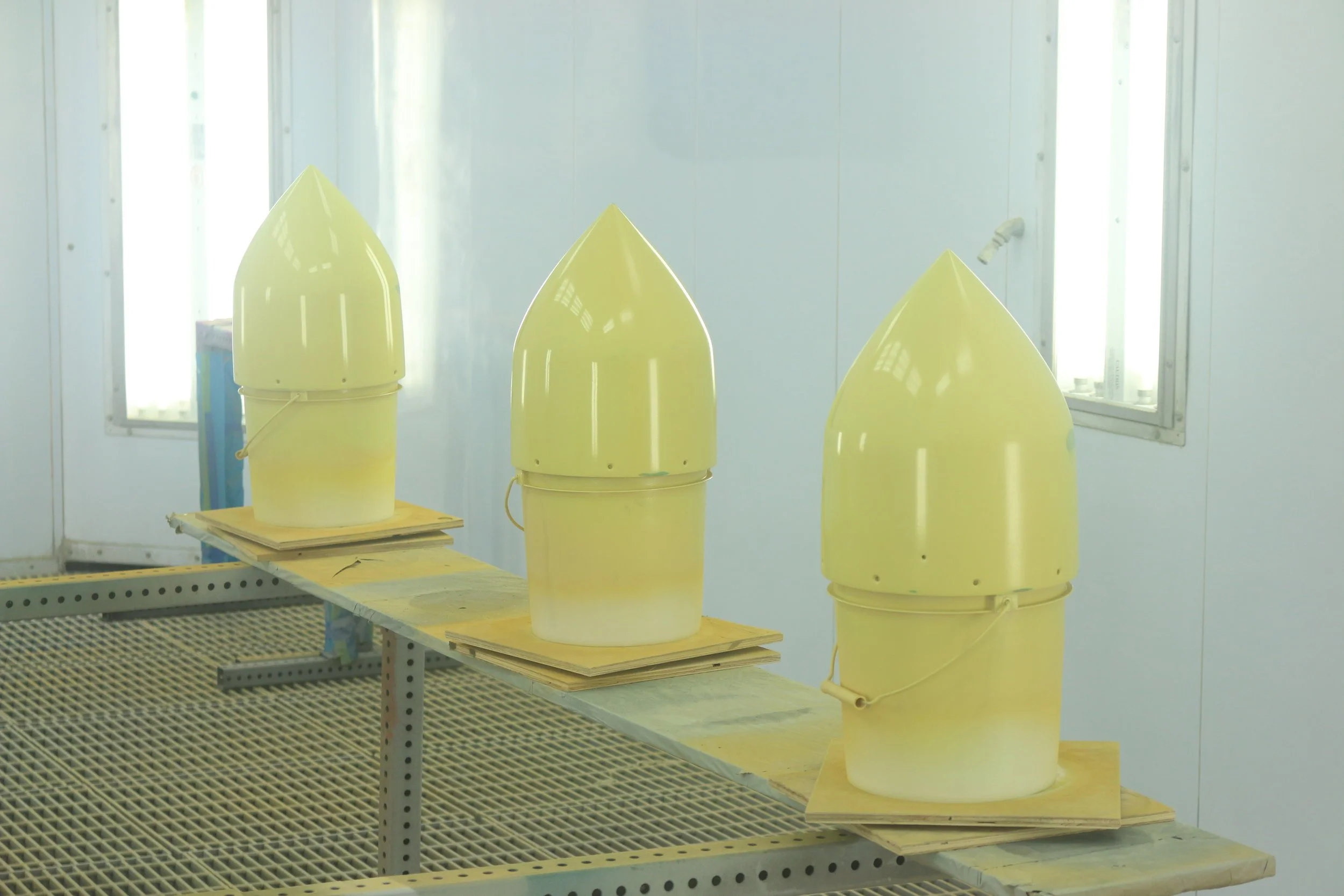 Three missile nose cones in a paint booth, drying on a work surface.